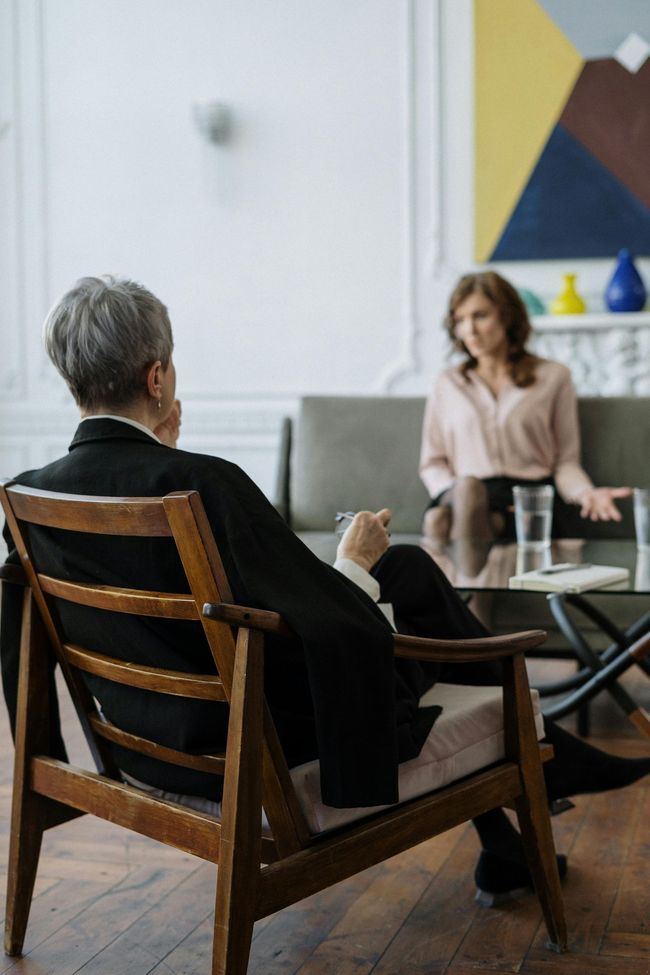 Two people seated across a table from one another; one offering support and advice while the other listens.
