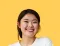Smiling Asian woman in a white shirt against a yellow backdrop.