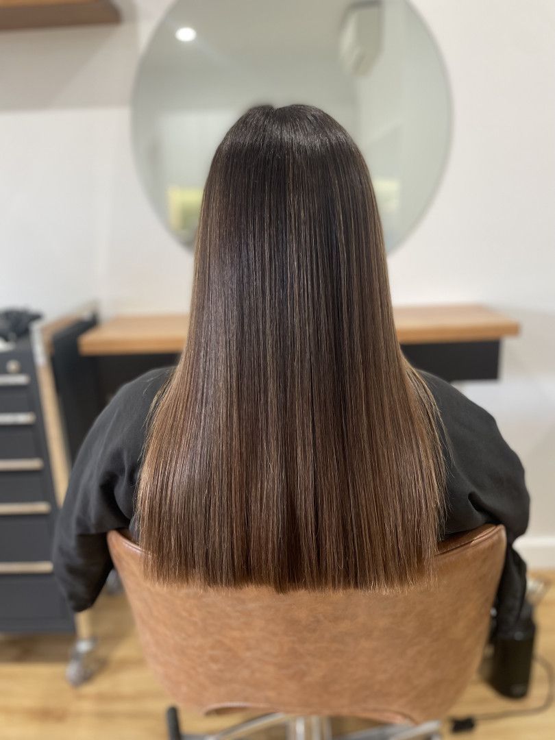 Person sitting in a salon chair with straight, brown hair, facing away — Clippers Hair Salon in Taree, NSW