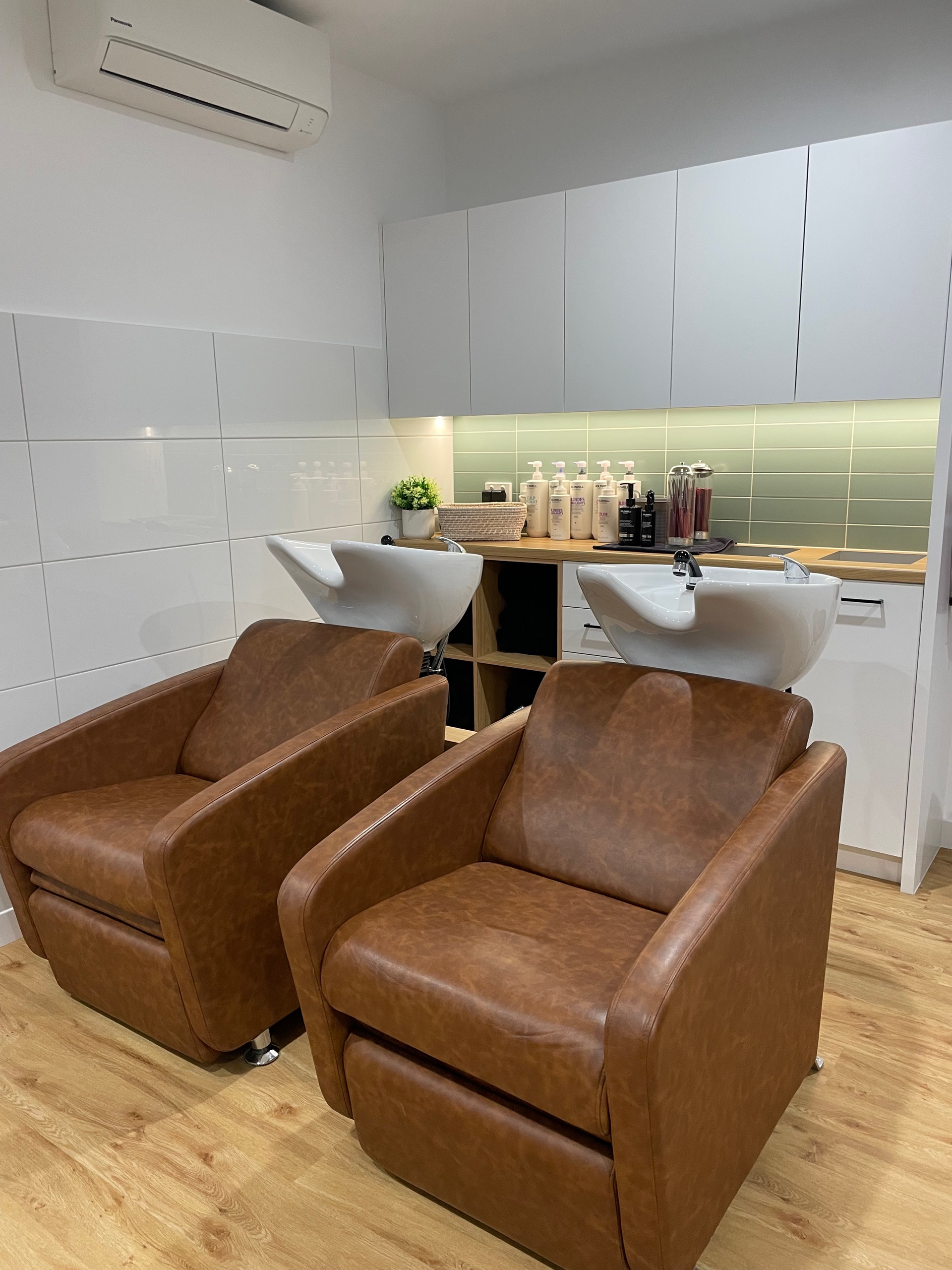 Two brown leather chairs in a hair salon next to shampoo bowls. White cabinets and a wooden floor — Clippers Hair Salon in Taree, NSW