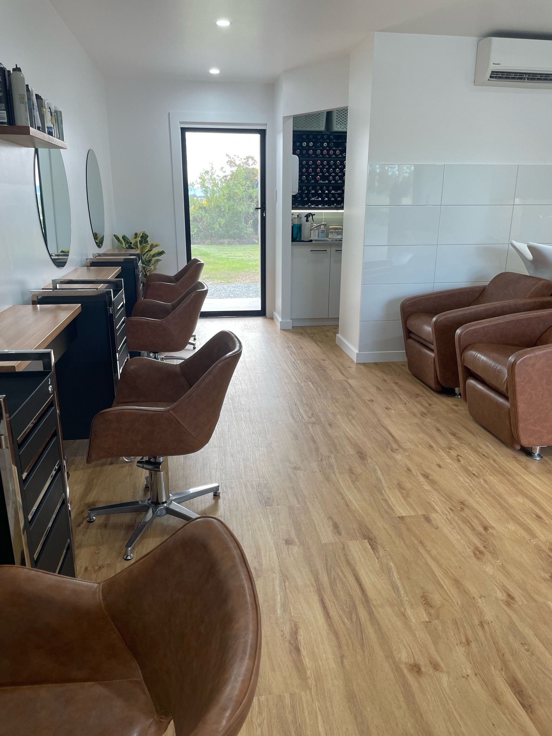 Hair salon interior with styling stations, brown leather chairs, and light wood flooring — Clippers Hair Salon in Taree, NSW