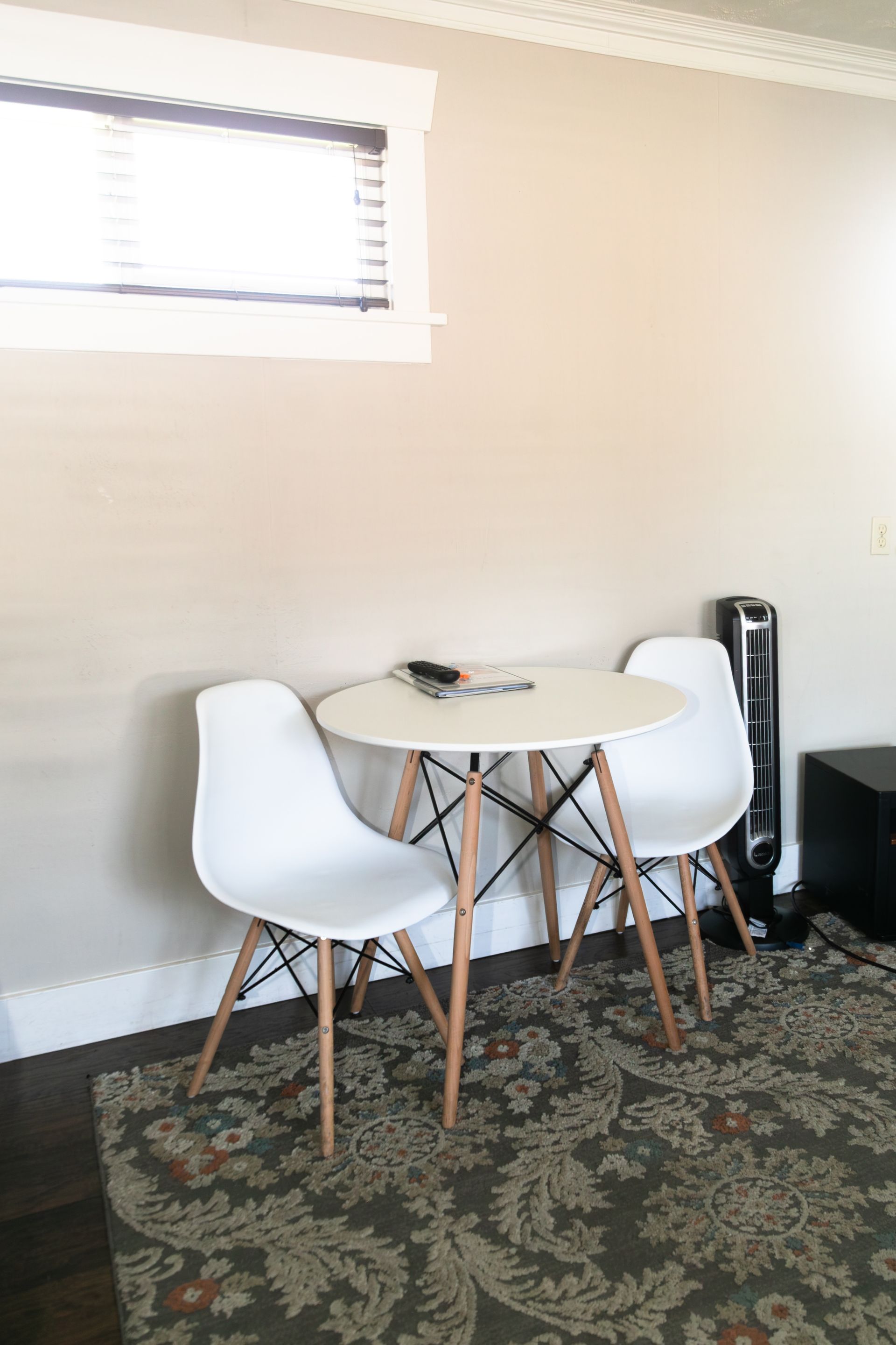 Small dining nook with two white chairs, round table, patterned rug, and a window.