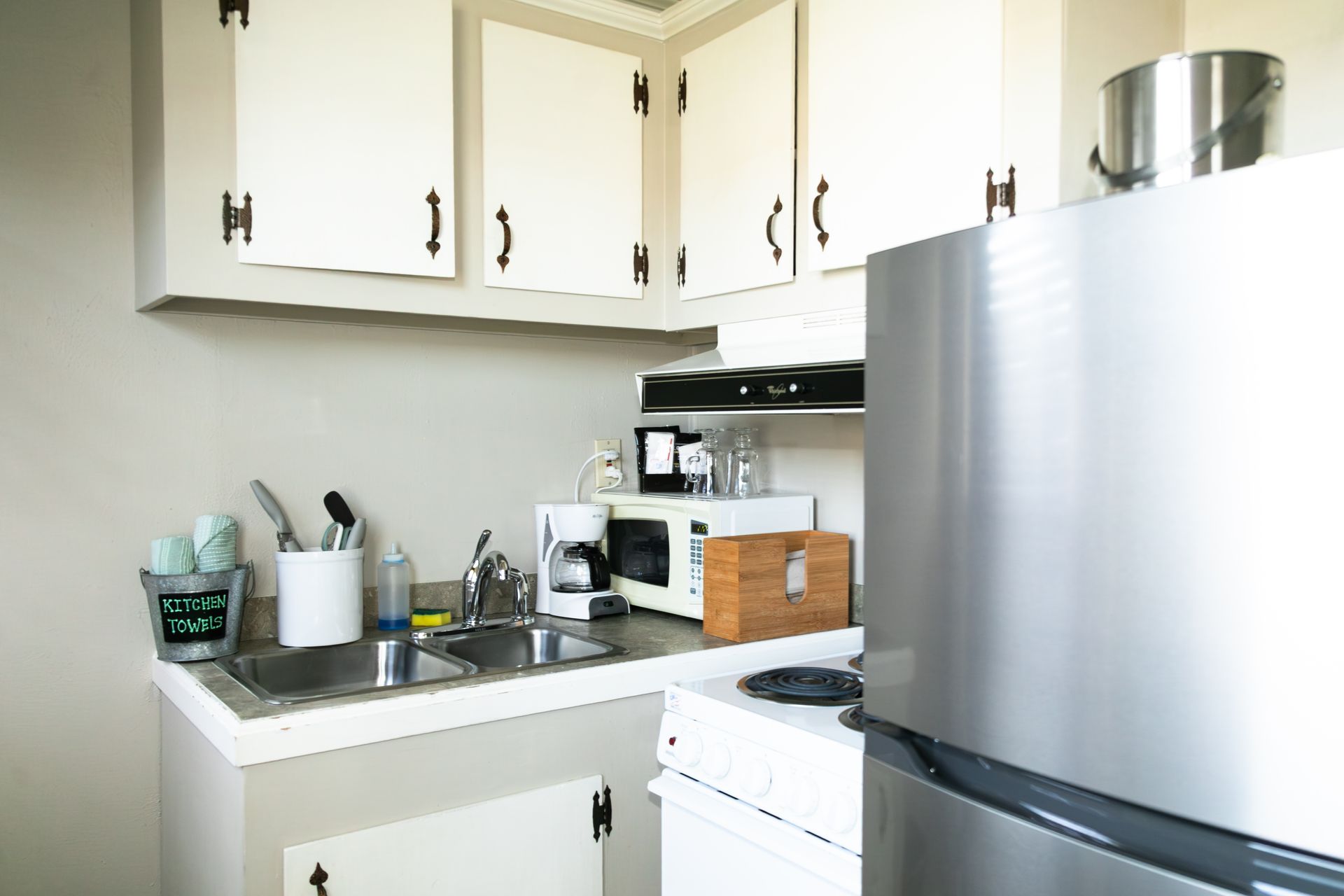 Small white kitchen with cabinets, sink, stove, and stainless-steel refrigerator.