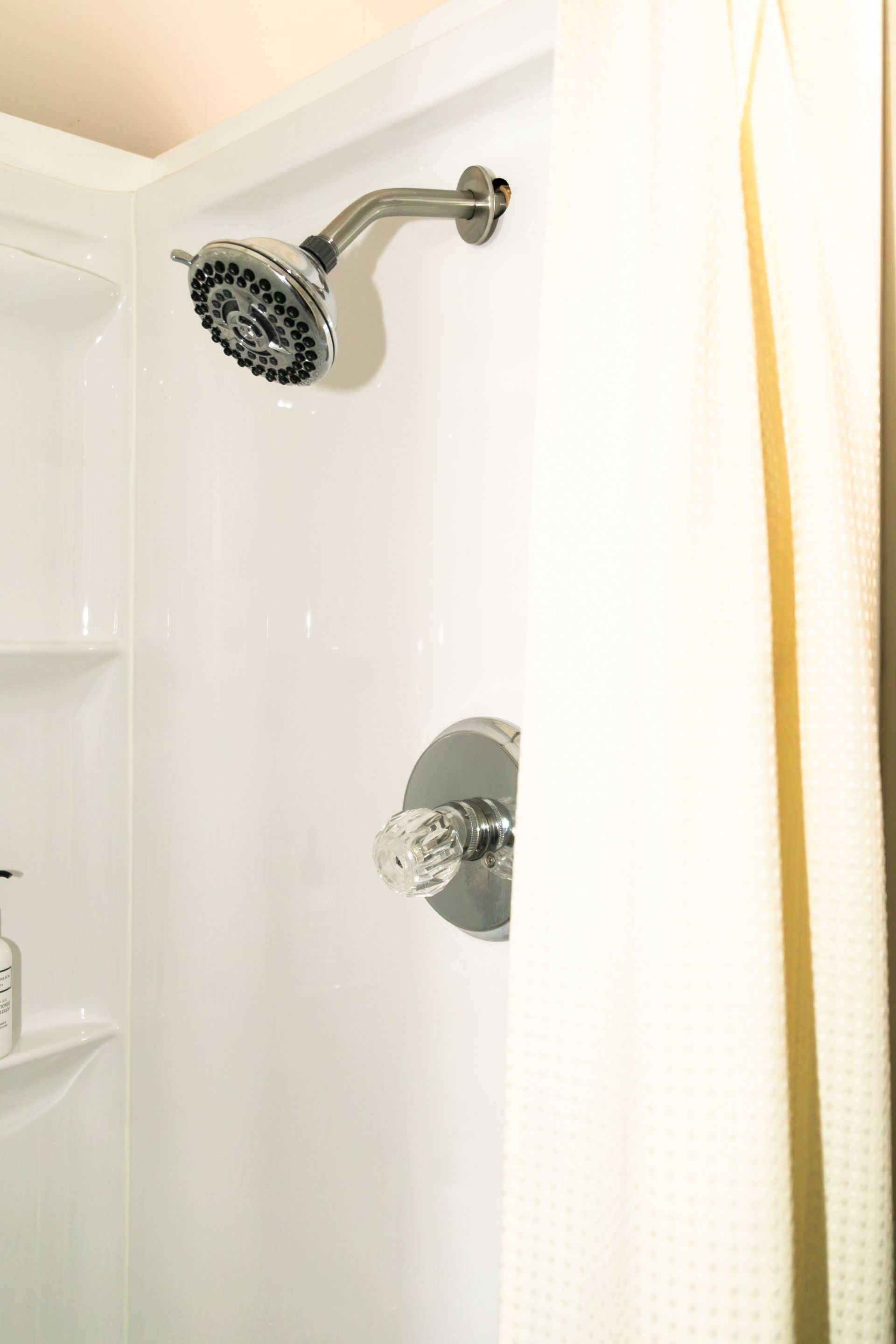 White shower stall with chrome showerhead and control knob, partially covered by a white curtain