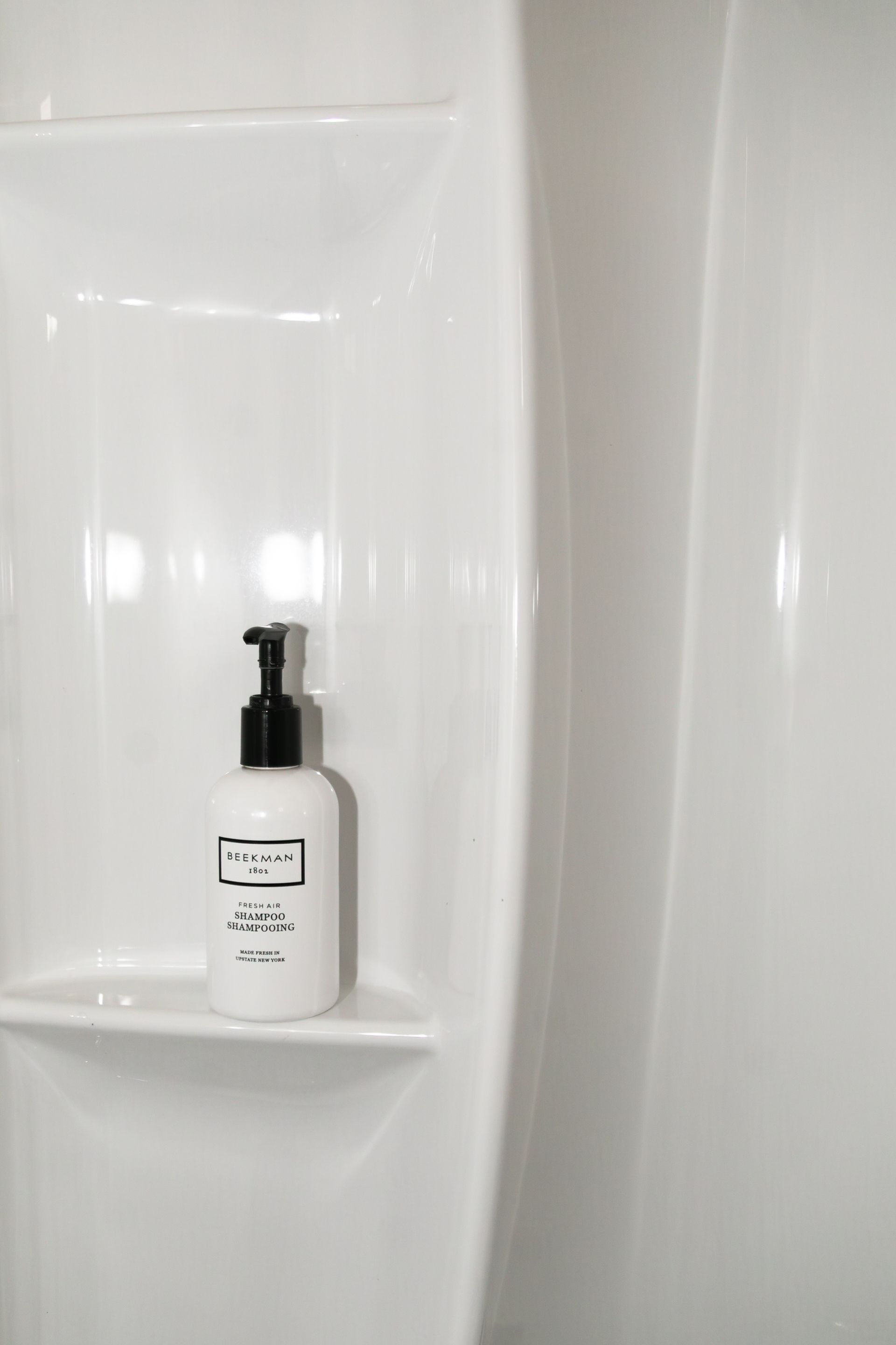 White shampoo bottle on a bathroom shower shelf against white tile.