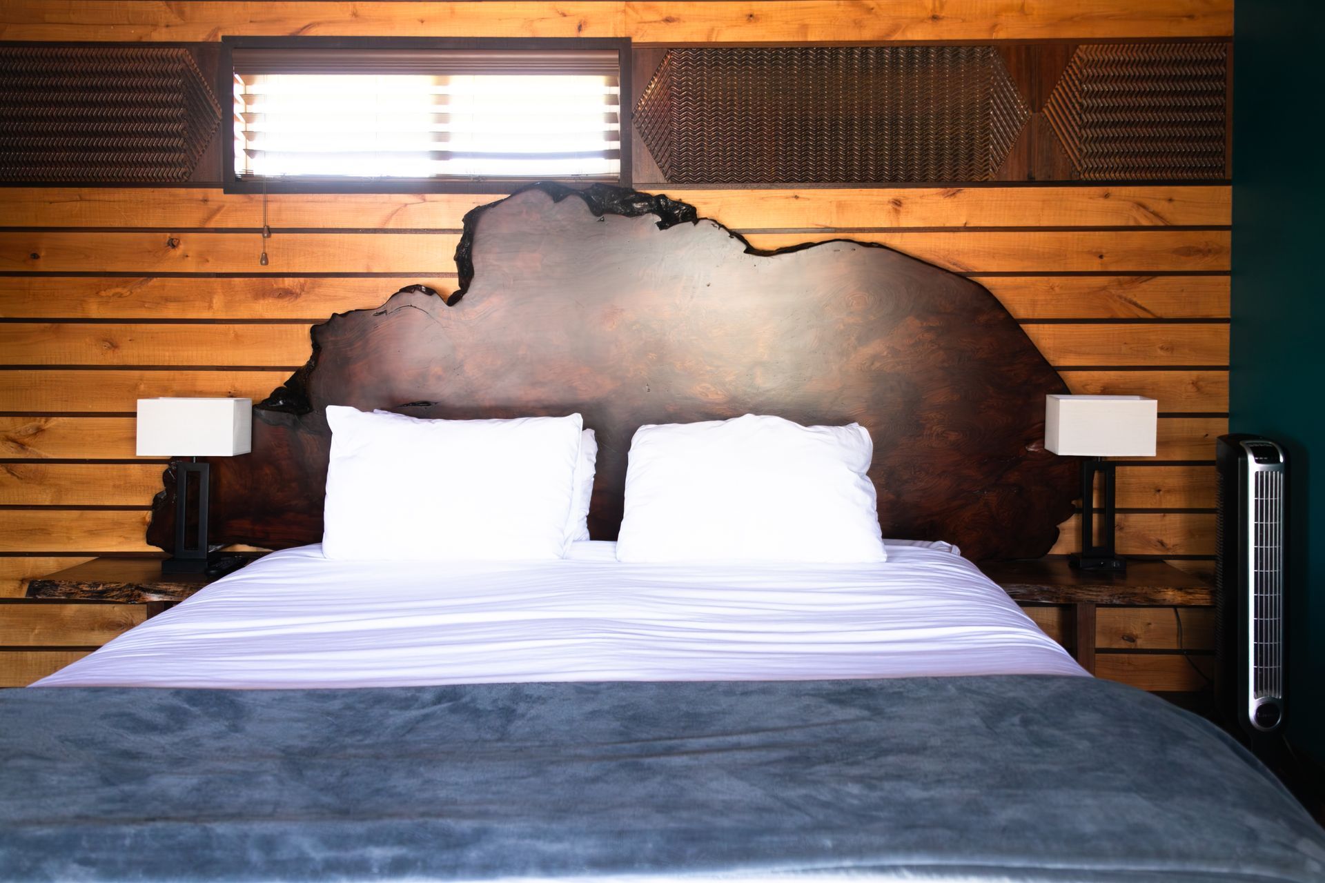 Bedroom with a wooden wall, white pillows, and a gray bedspread under a lit window headboard