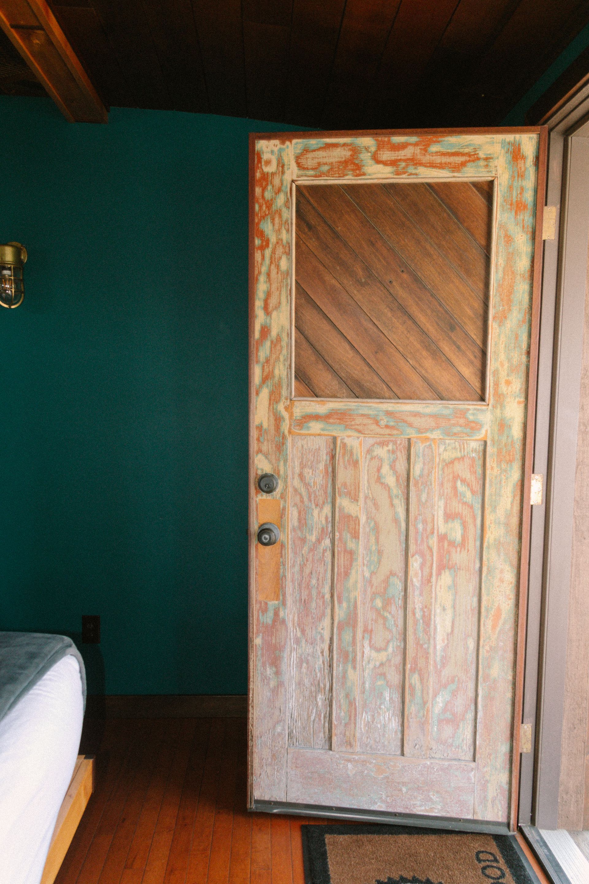 Rustic white wooden door with a square window in a dark green room