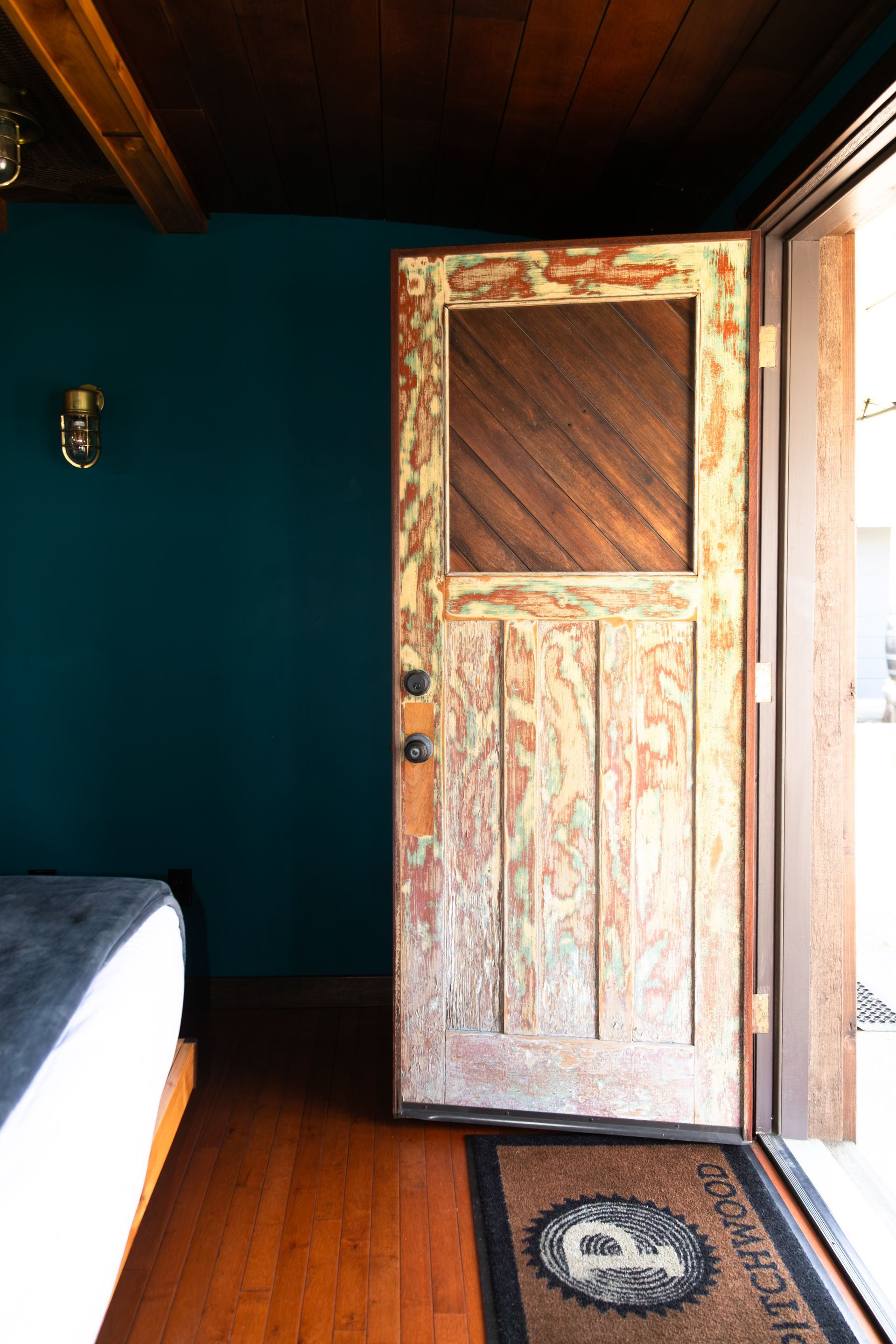 Rustic wooden door ajar in a teal-walled room with a bed and patterned rug