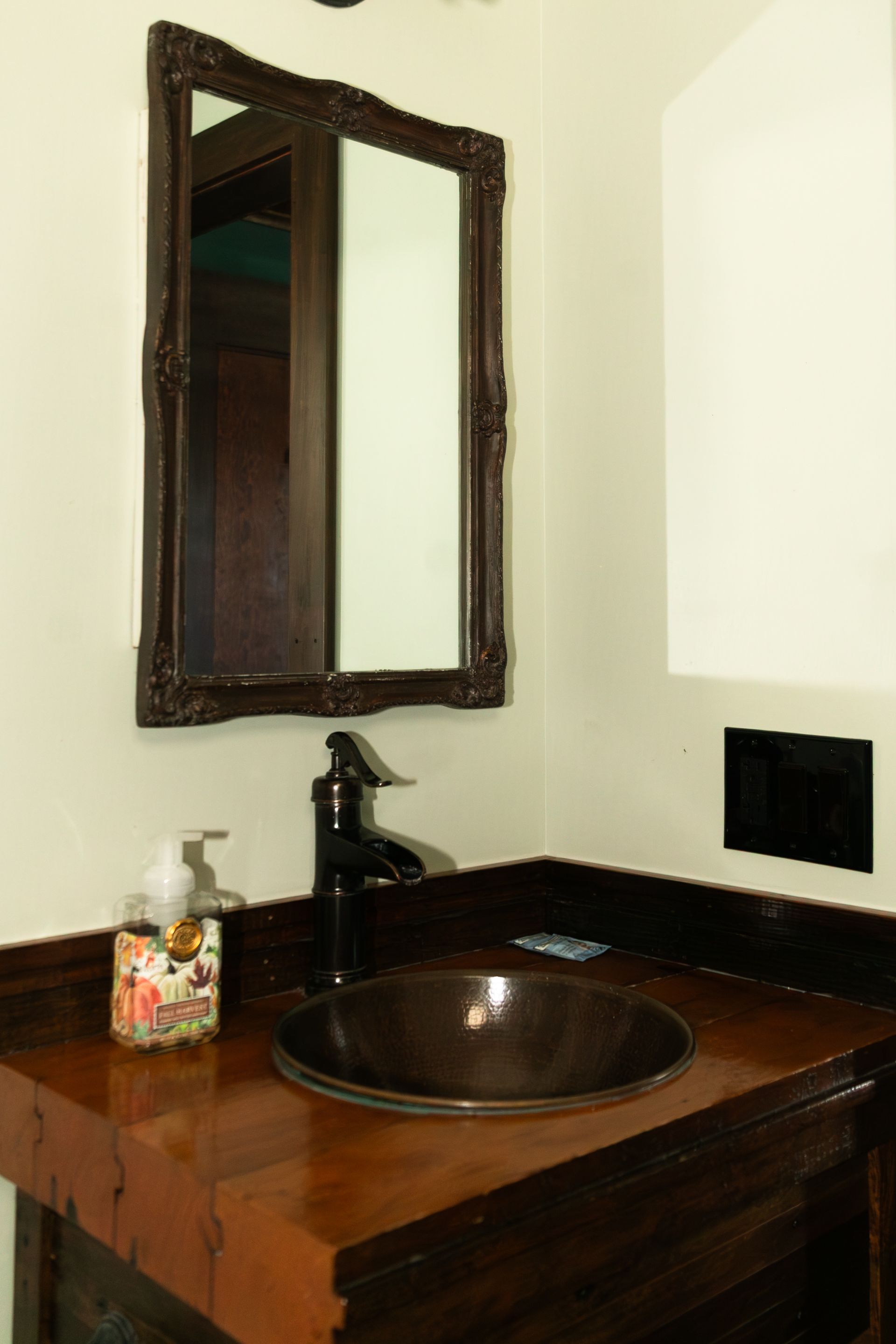 Bathroom vanity with dark wood counter, round sink, black faucet, and framed mirror on a cream wall