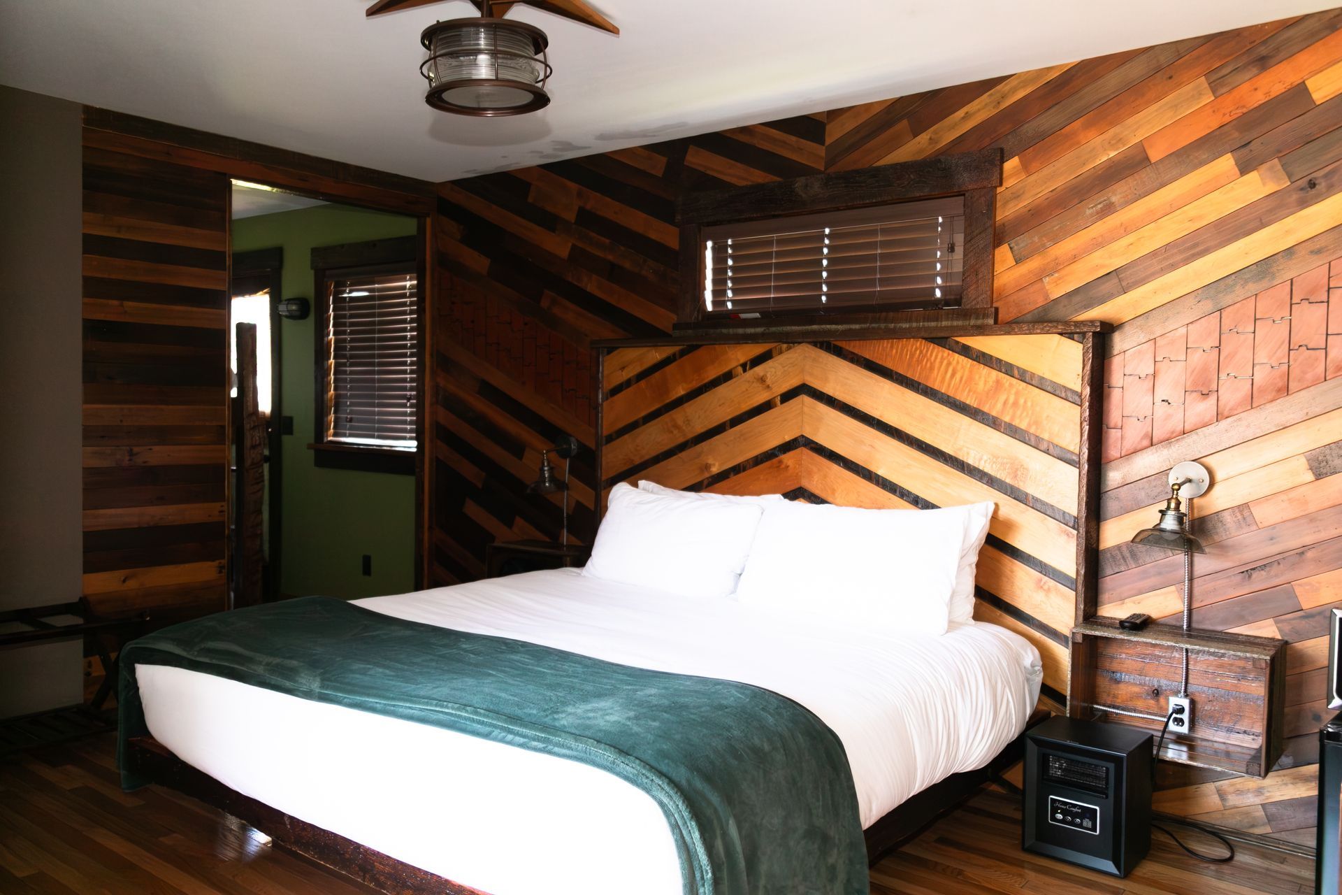 Cozy rustic bedroom with a white bed, green blanket, and wood-paneled walls