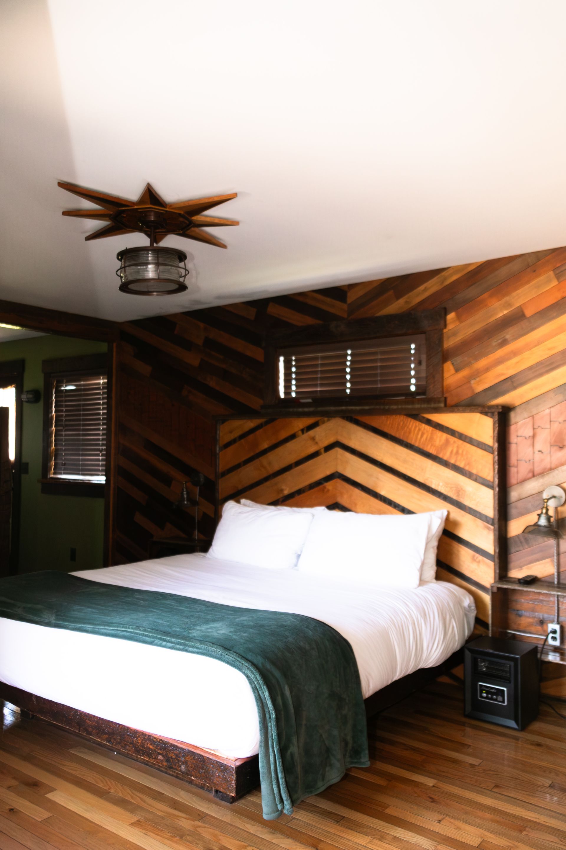 Cozy wooden bedroom with a white bed, dark green throw, and ceiling fan light