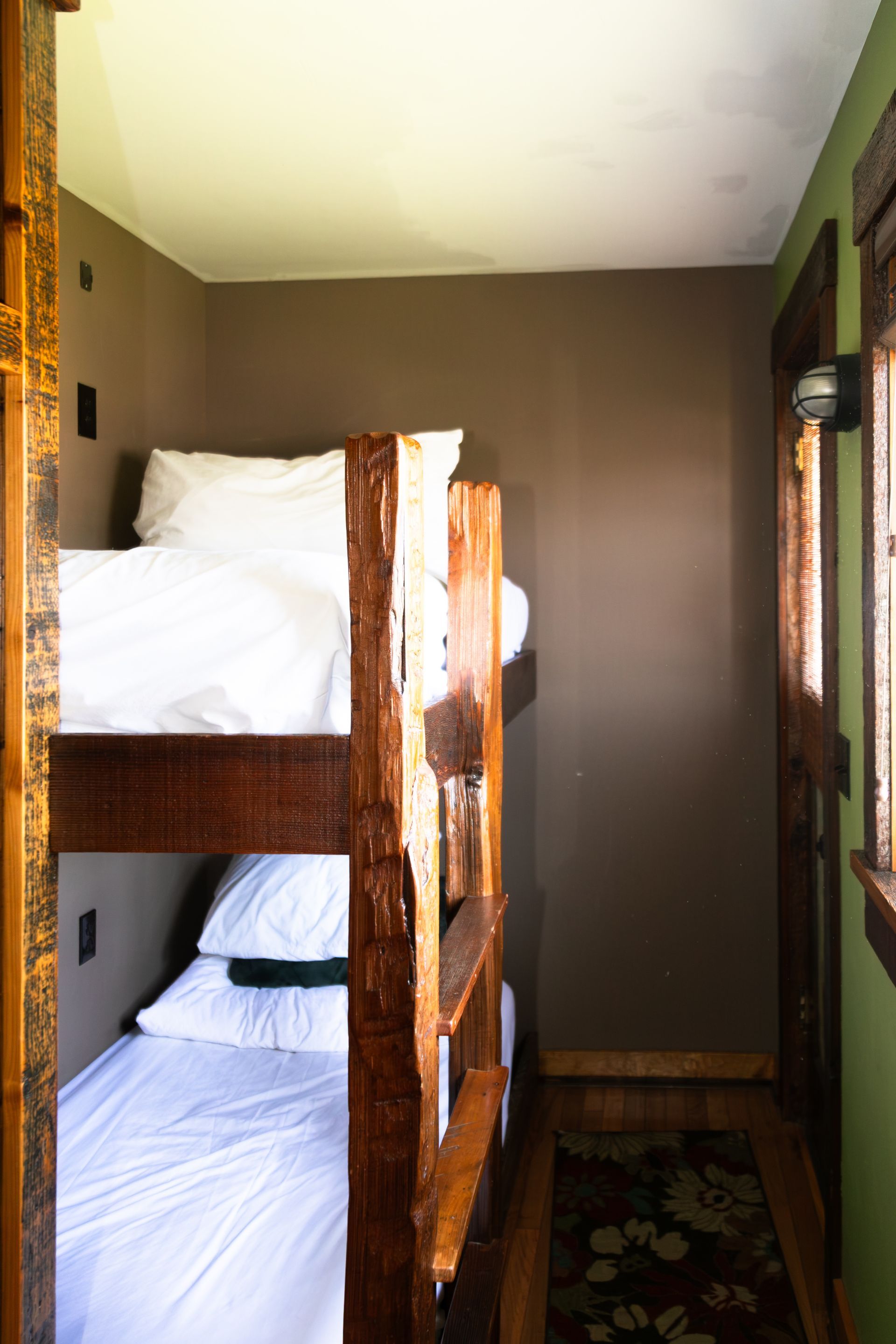 Narrow hallway with wooden bunk beds, white bedding, and a patterned rug along the floor