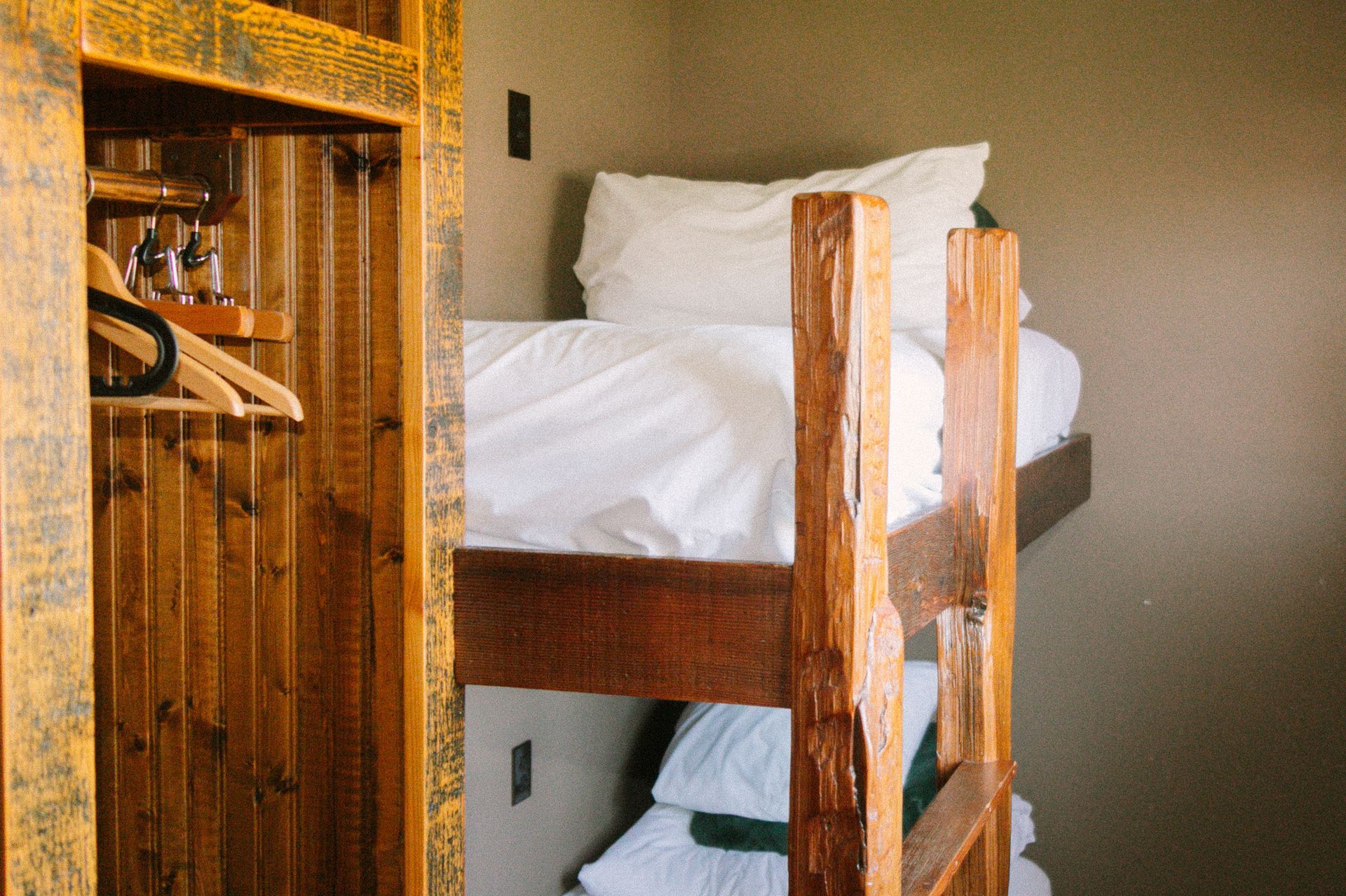 Wooden bunk bed with white bedding beside an open closet in a small room