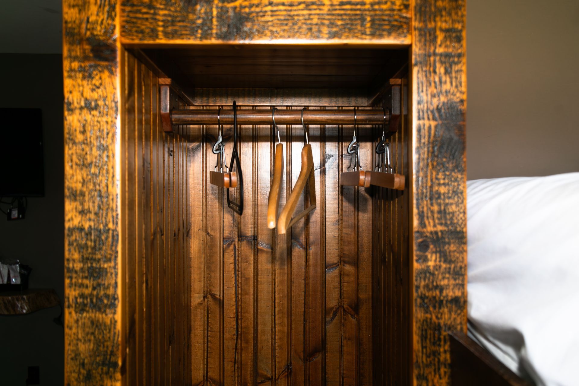 Wooden closet with hanging clothes and a white bed beside it