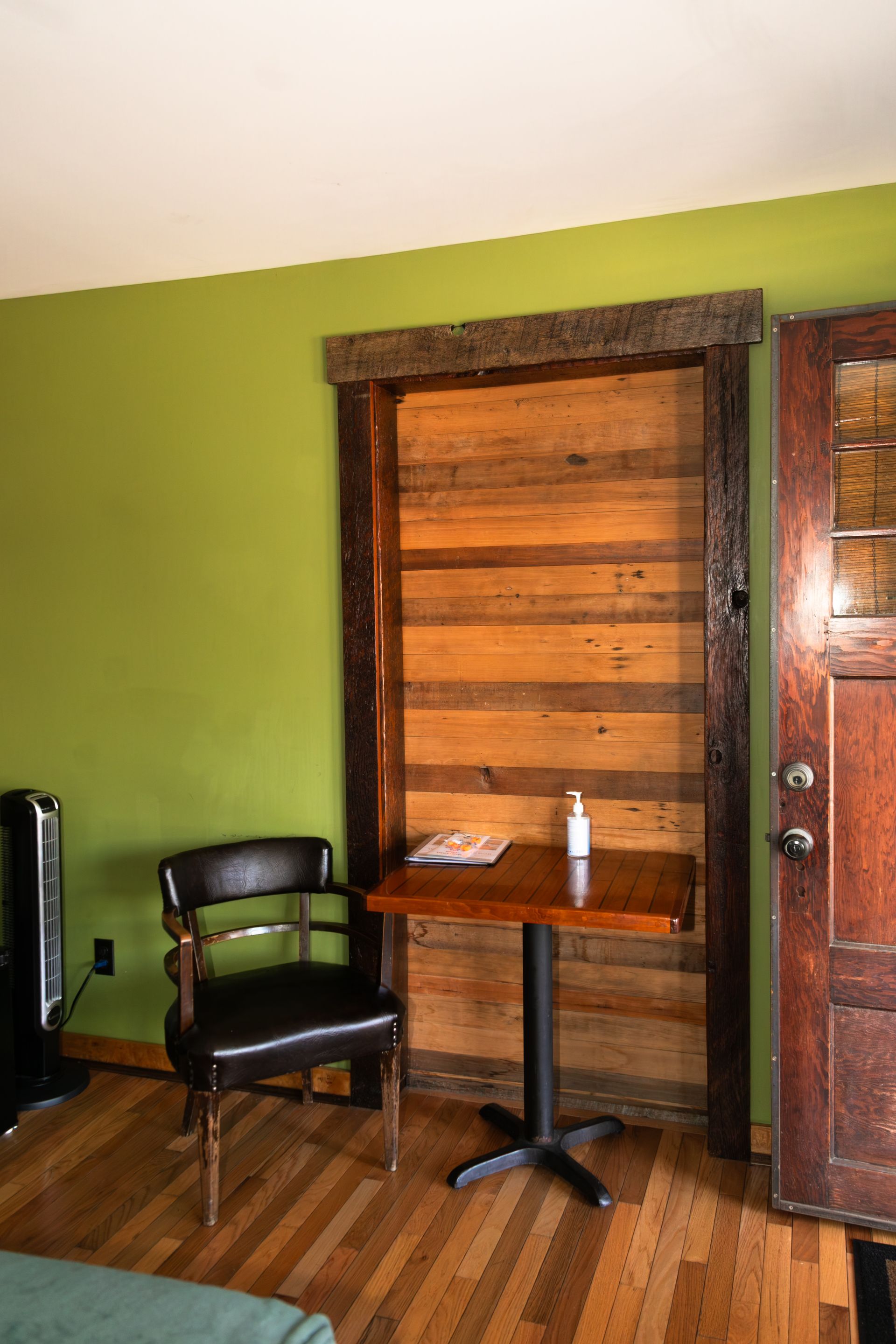 Small room with green walls, wooden doors, a chair, and a small table with a bottle.