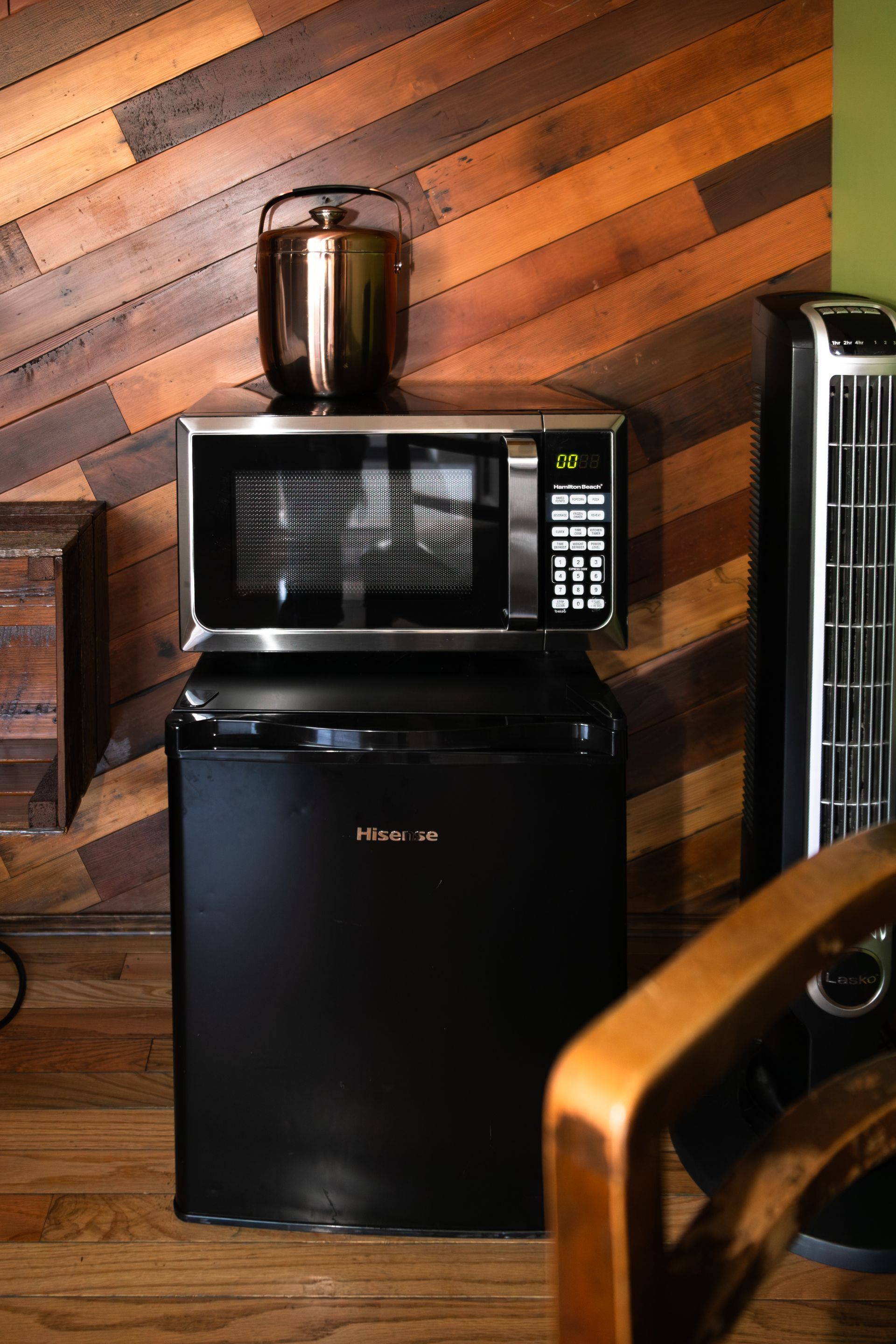 Microwave on a black mini fridge in a room with diagonal wood paneling and a tall heater nearby