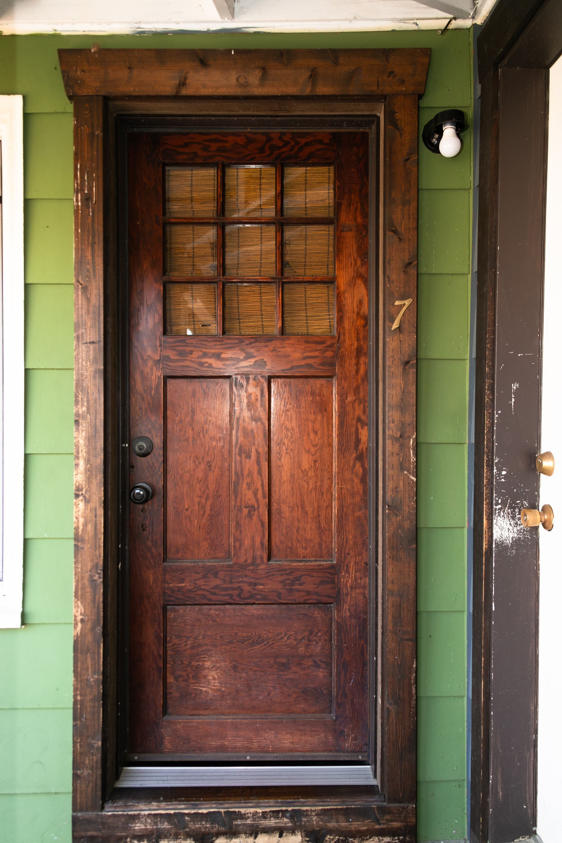 Wooden front door with a dark frame and green exterior wall, viewed from the porch