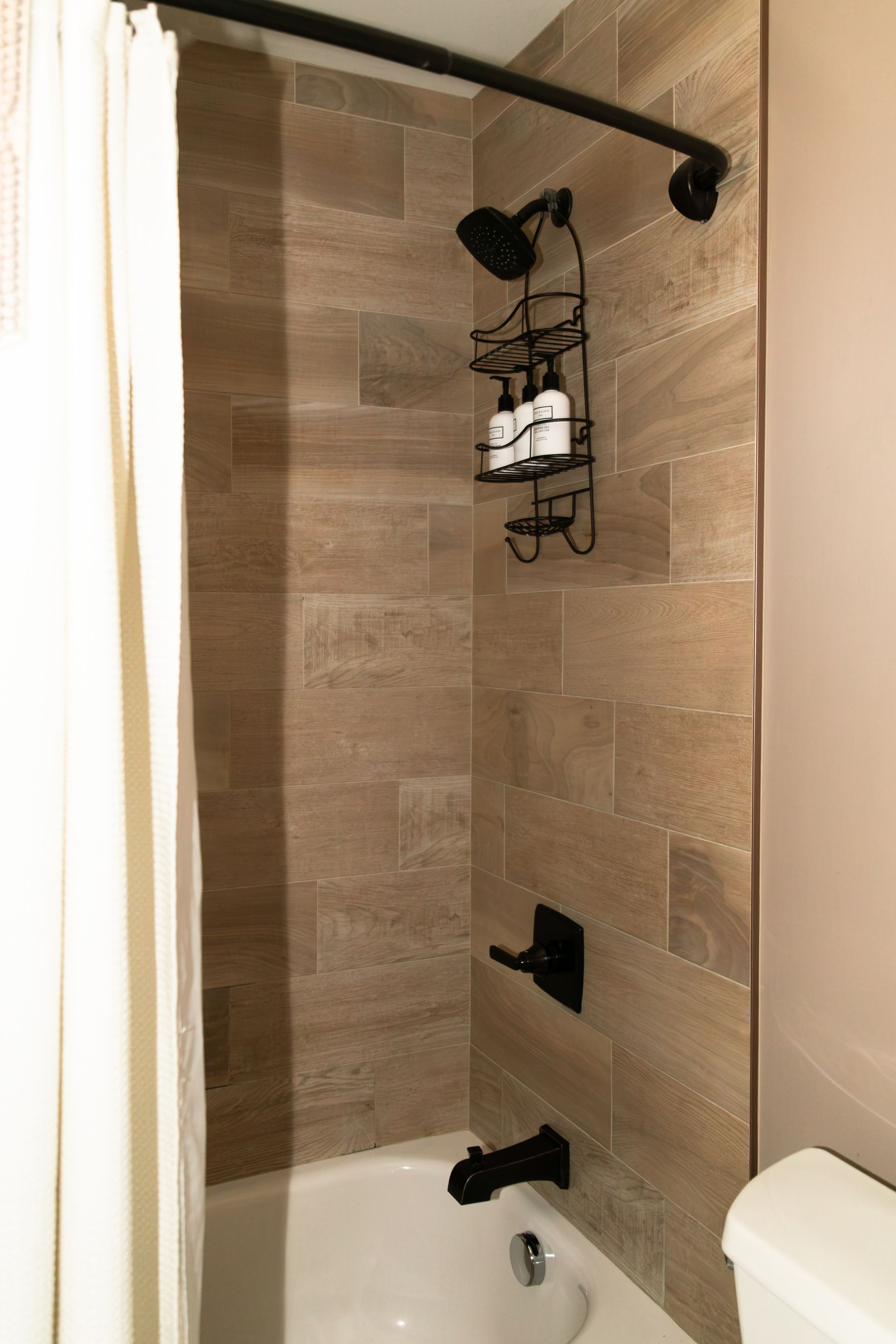 Small beige-tiled shower with black fixtures, wall shelf, and a curtain.