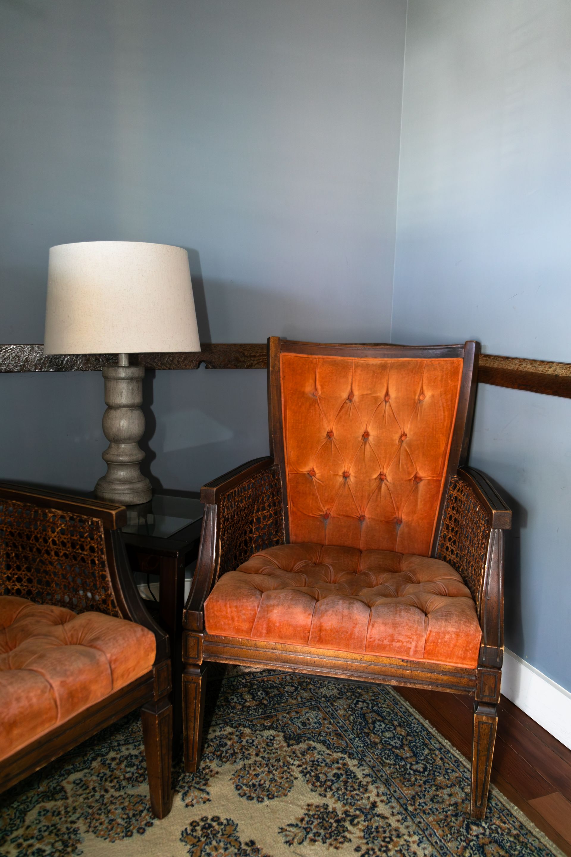 Two orange upholstered chairs beside a floor lamp in a blue-gray corner