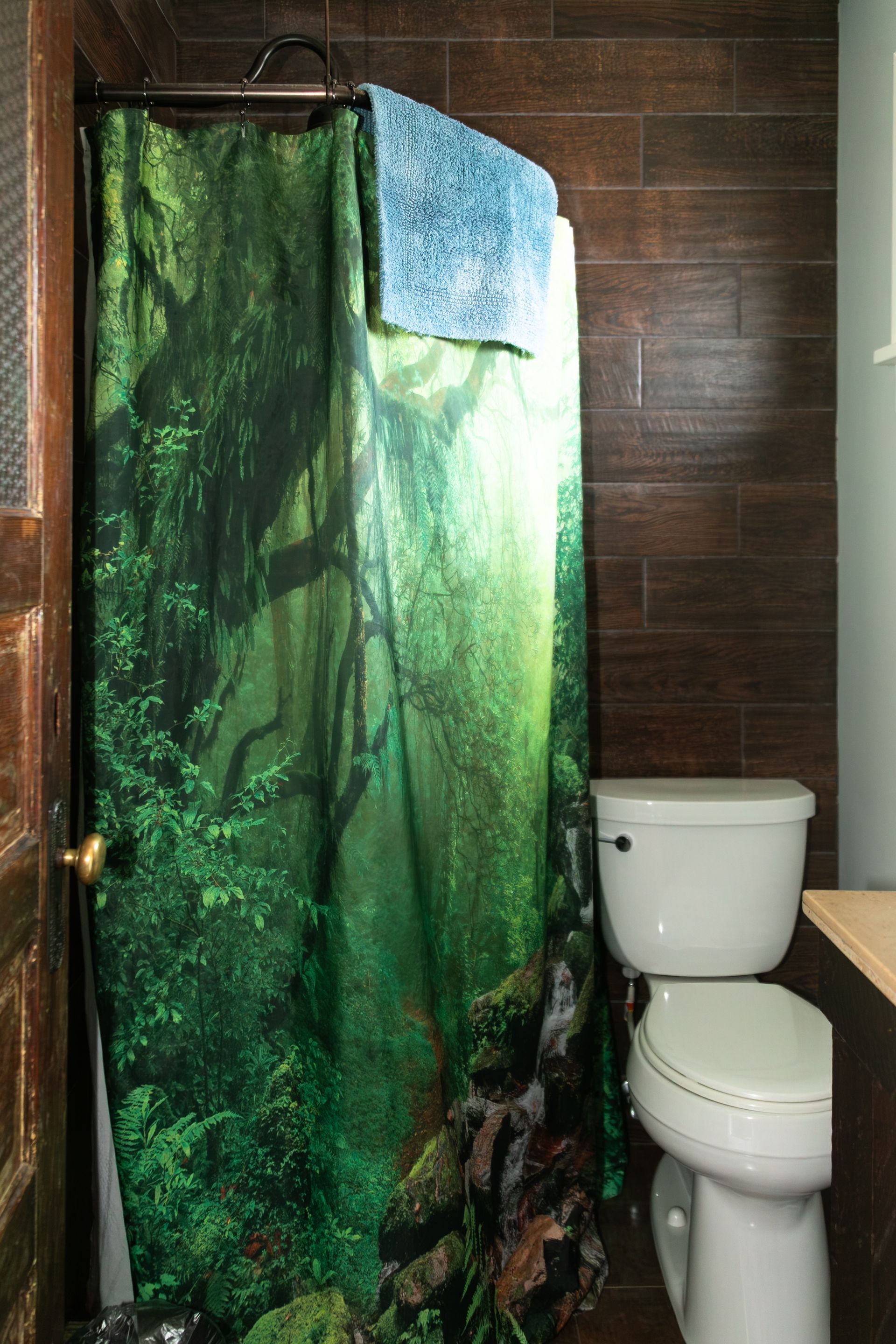 Green rainforest shower curtain in a bathroom beside a white toilet.