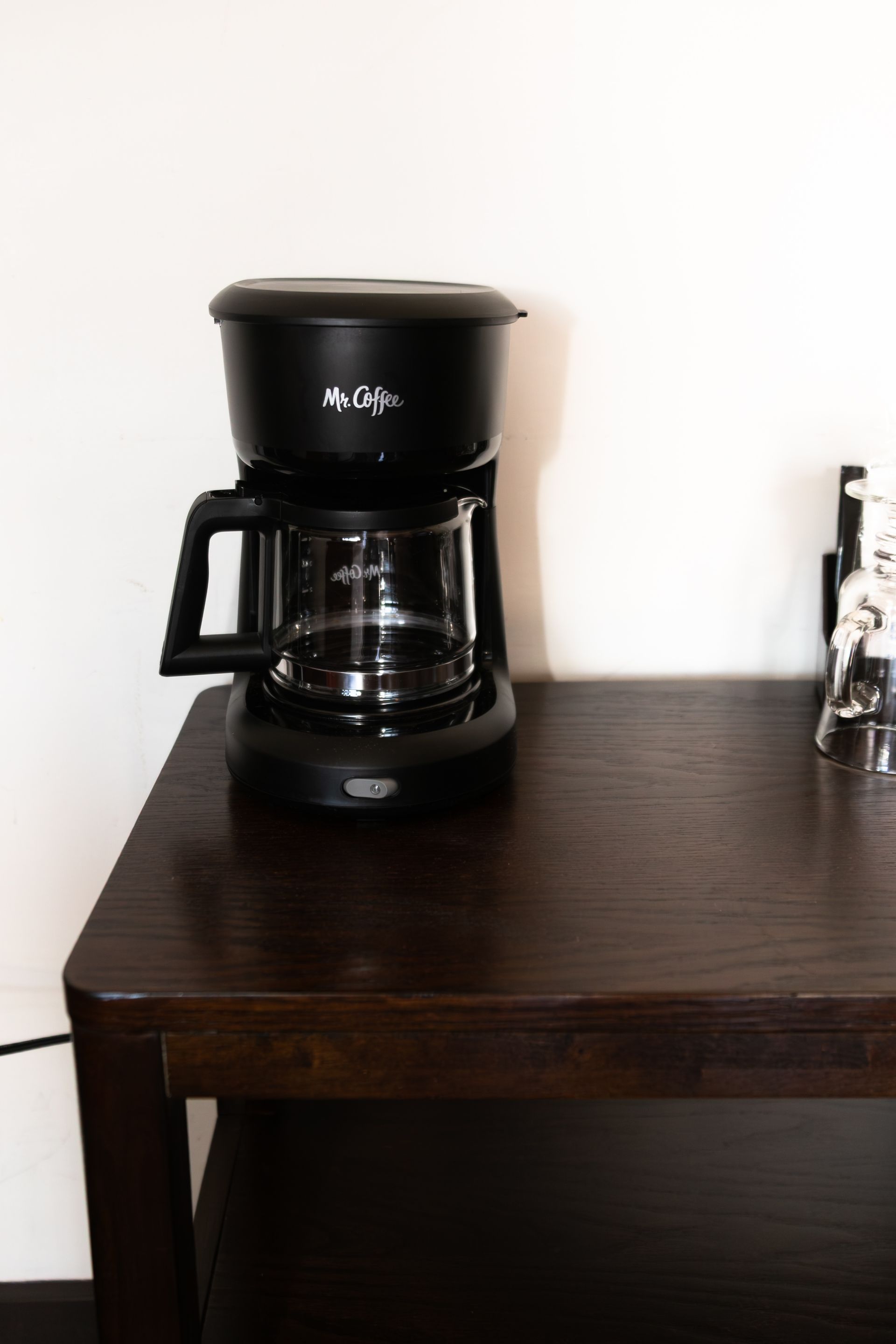 Black coffee maker on a dark wooden table against a white wall.