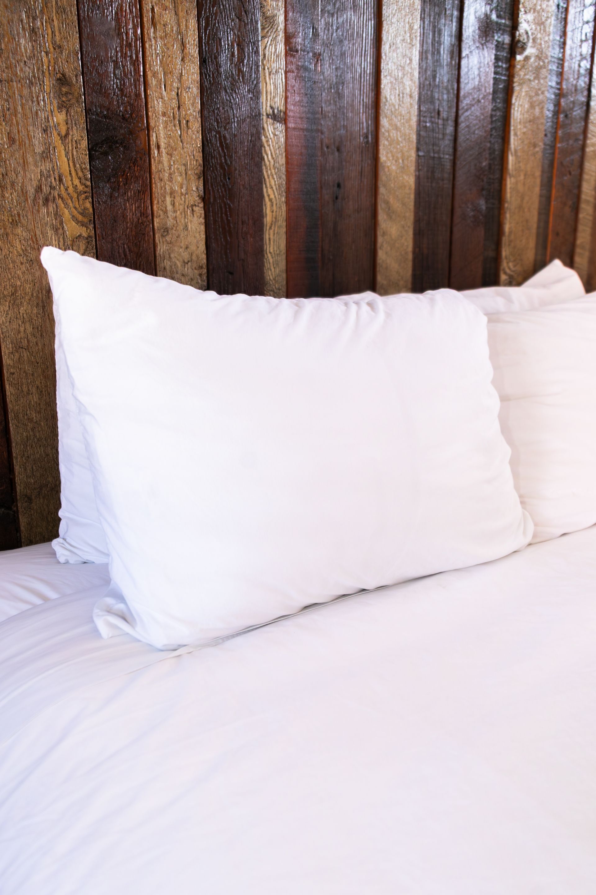 White pillows on a neatly made bed with a dark wooden headboard