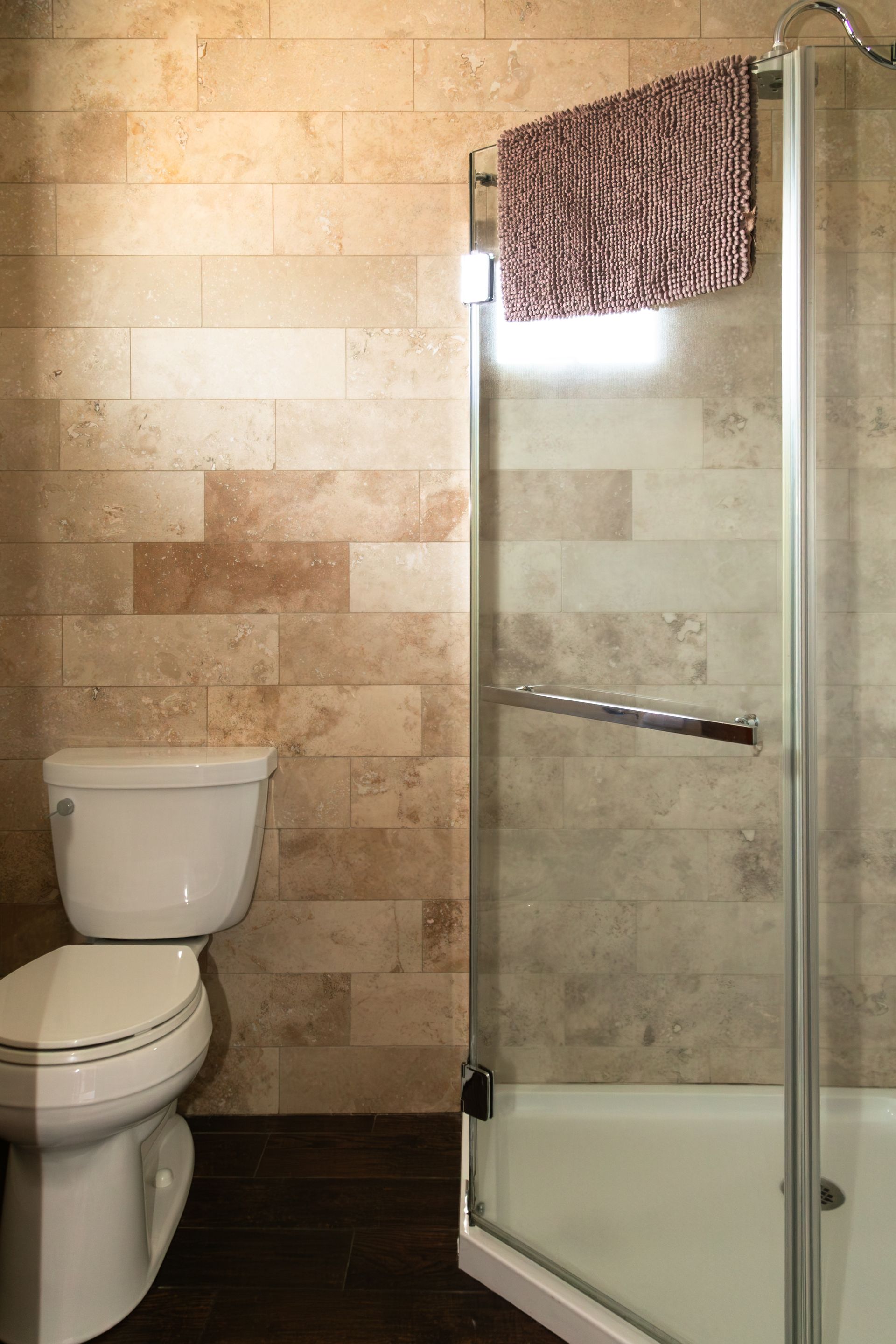 Small bathroom with beige tile, a toilet, and a glass shower enclosure with a towel hanging on top.