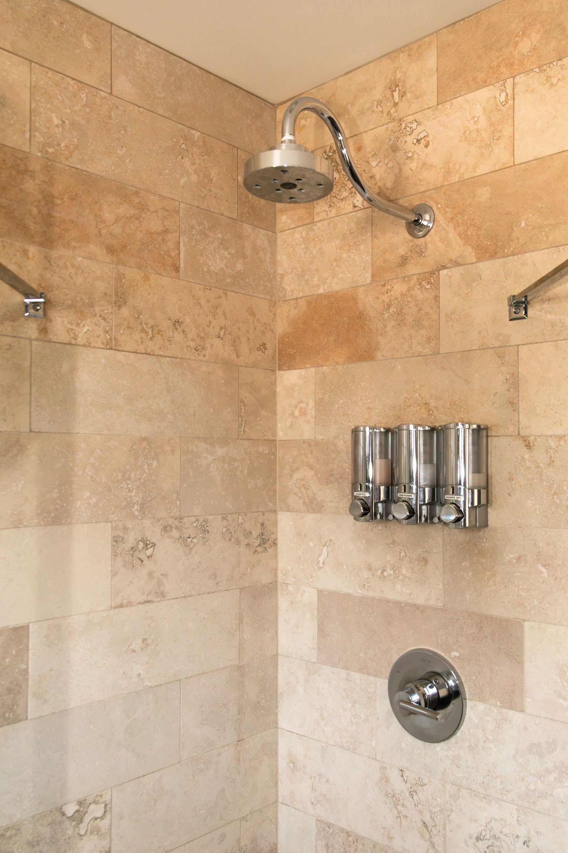 Stone-tiled shower with chrome showerhead and body spray controls