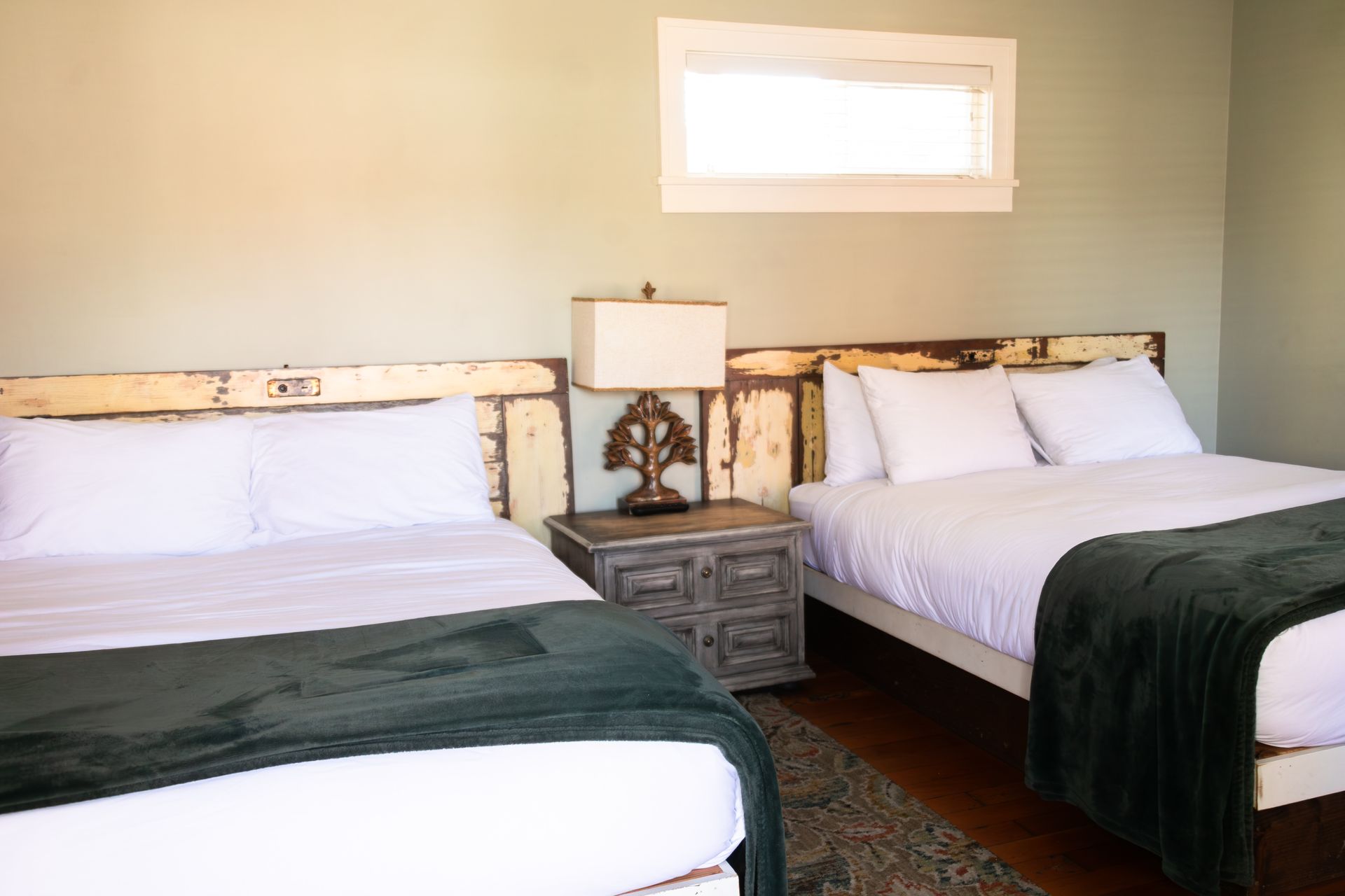 Two beds in a beige bedroom with a bedside lamp and small window
