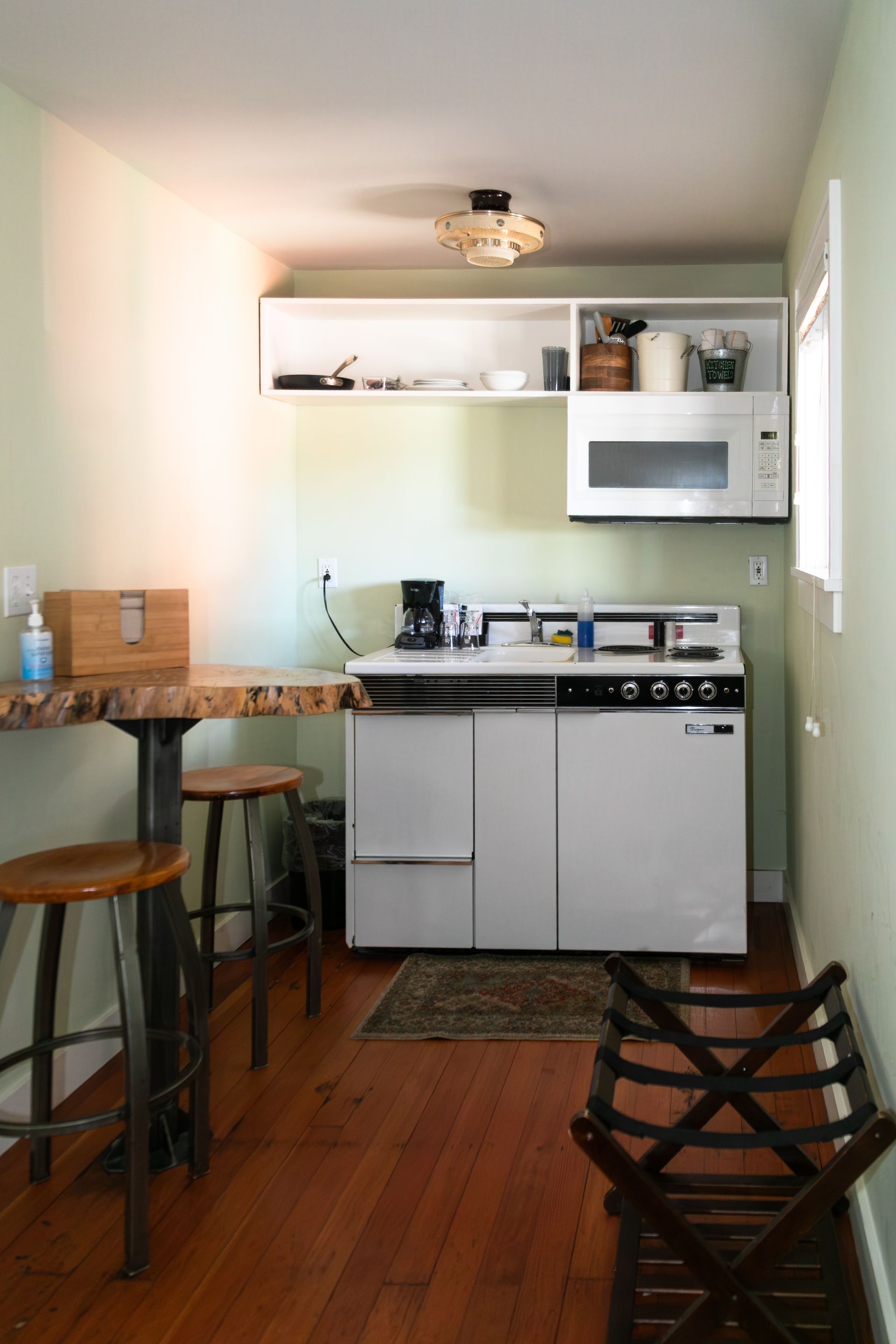 Narrow kitchen with white cabinets, wood floor, stove, microwave, and a small dining counter with stools.