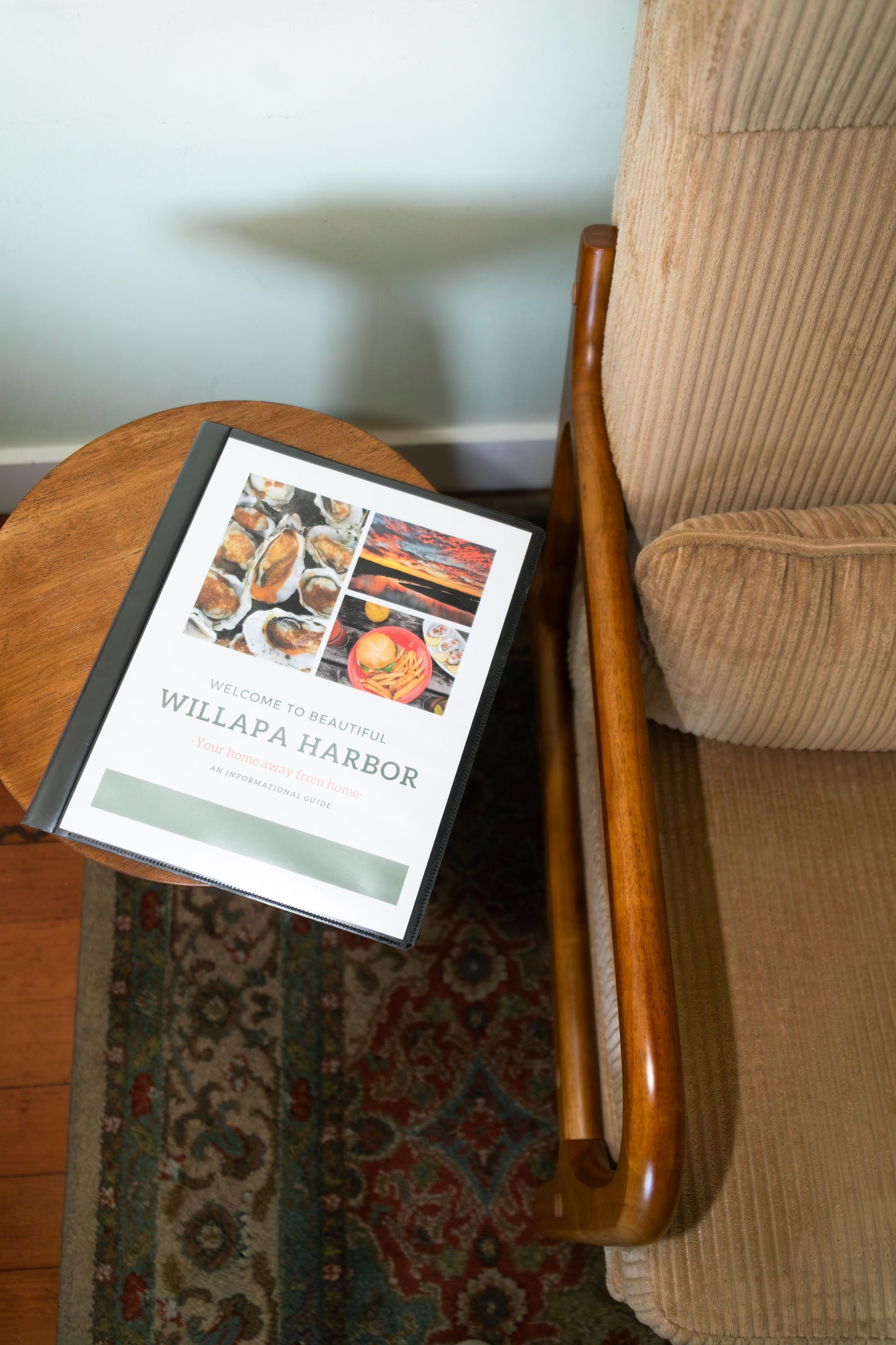 Book on a brown chair beside a tan sofa, with a patterned rug underneath.