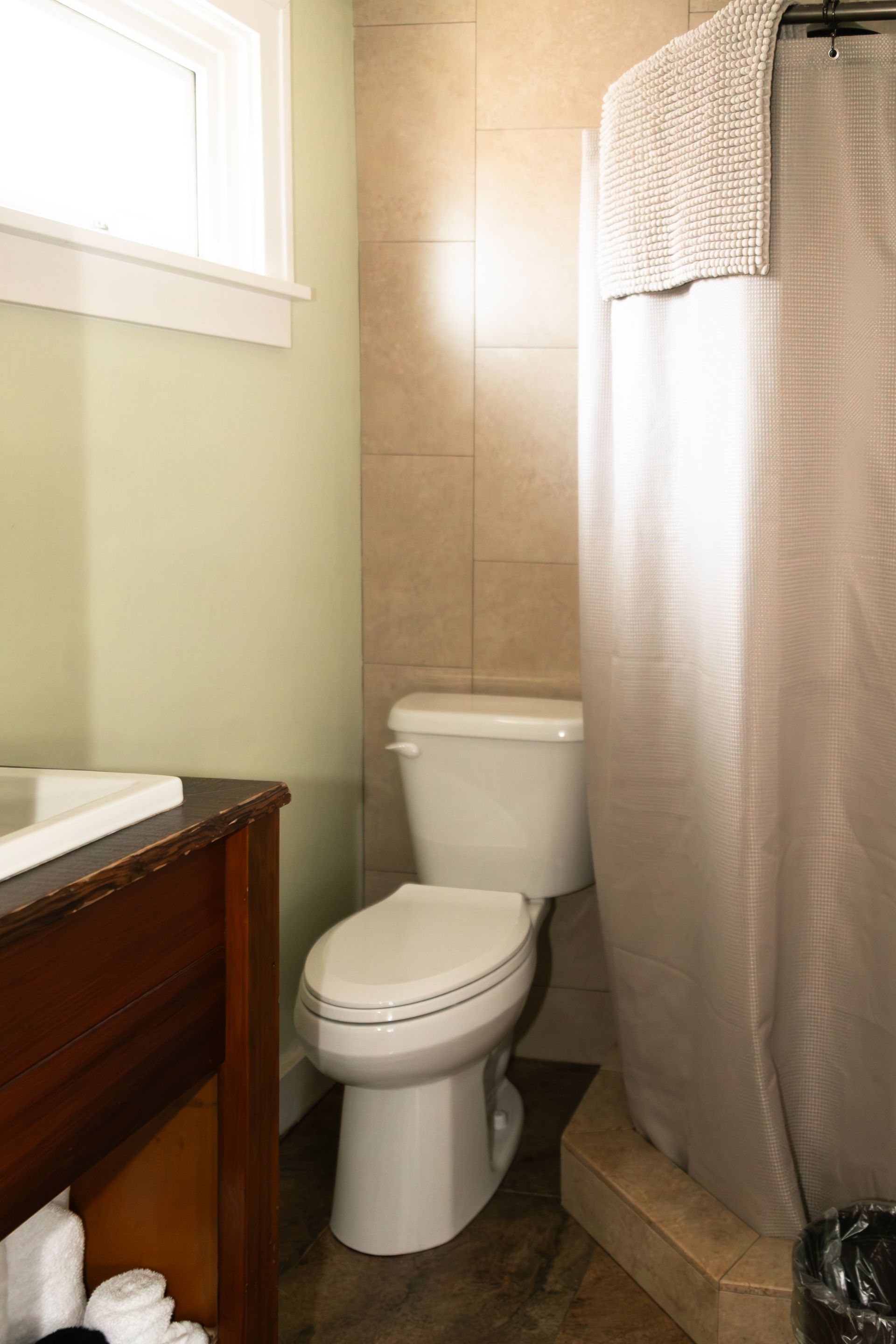 Small bathroom with a toilet, shower curtain, sink vanity, and window.