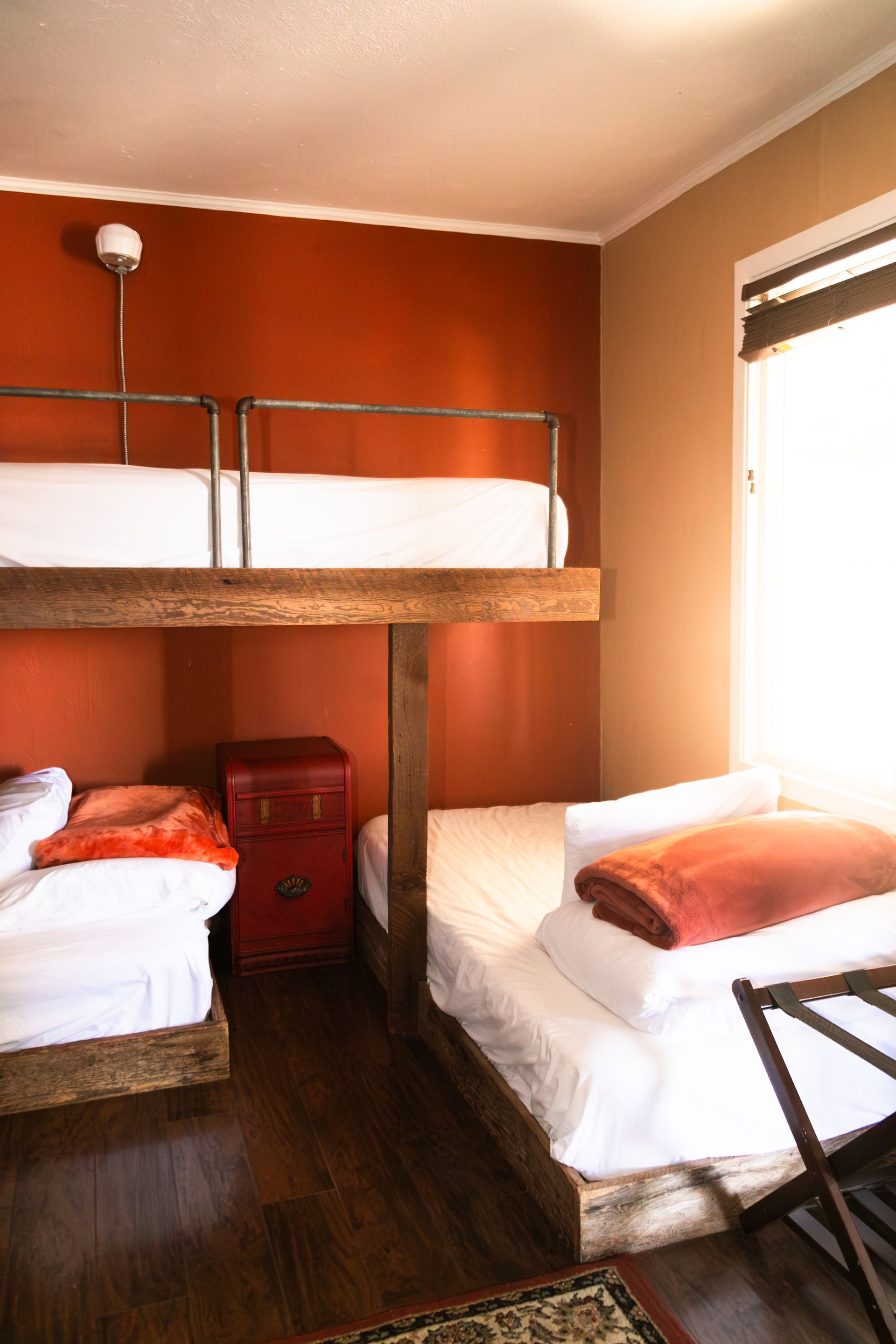 Small bedroom with two single beds, a bunk bed, red walls, and bright window light