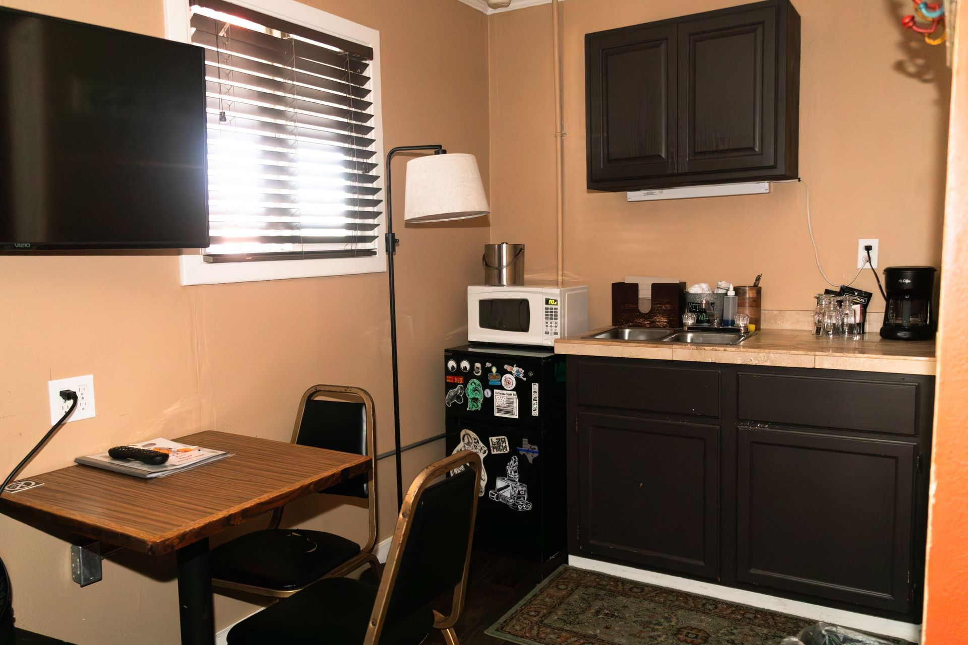 Small kitchenette with black cabinets, microwave, coffee maker, and a table by a window.