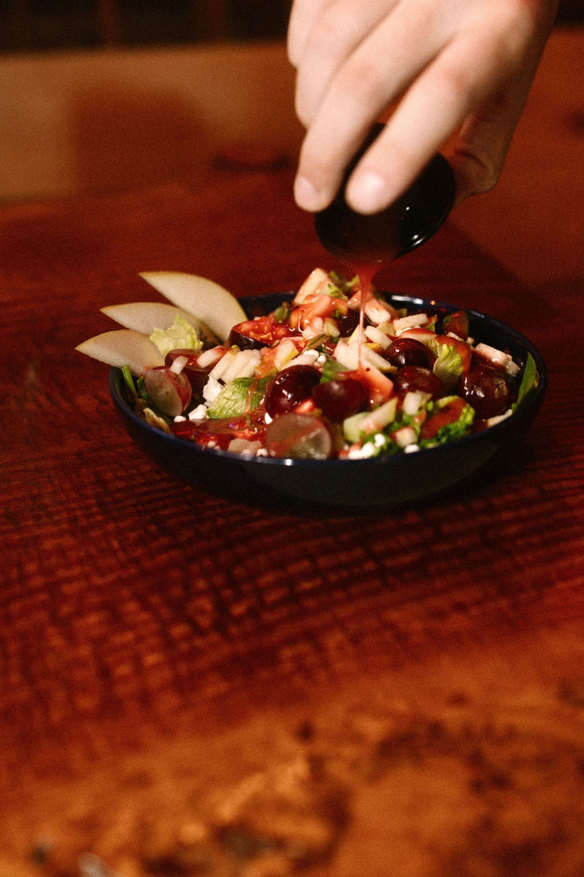 Hand placing lemon wedges into a small bowl of colorful salad on a wooden table