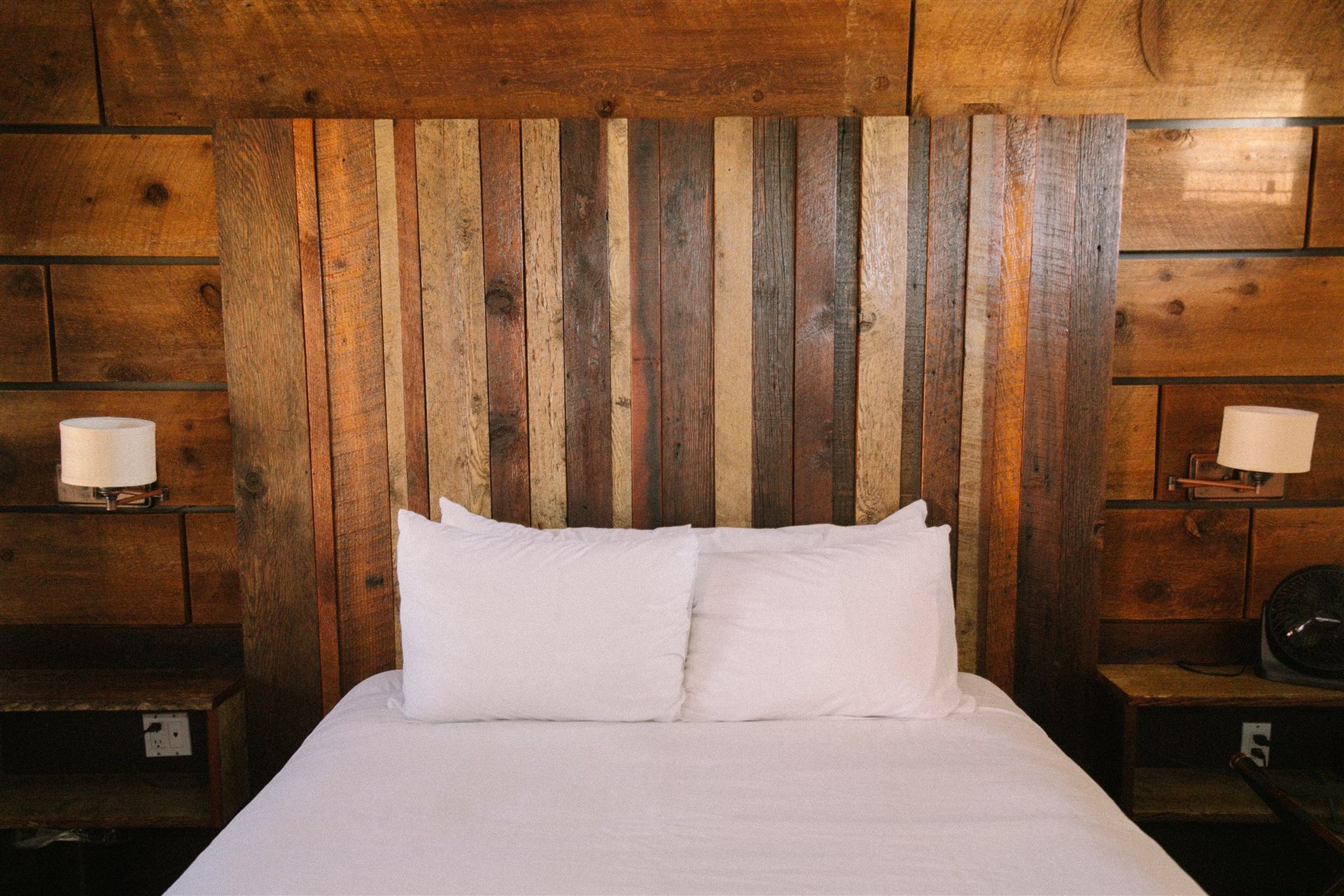 Neatly made bed with white pillows against a rustic wood-paneled headboard in a cozy bedroom
