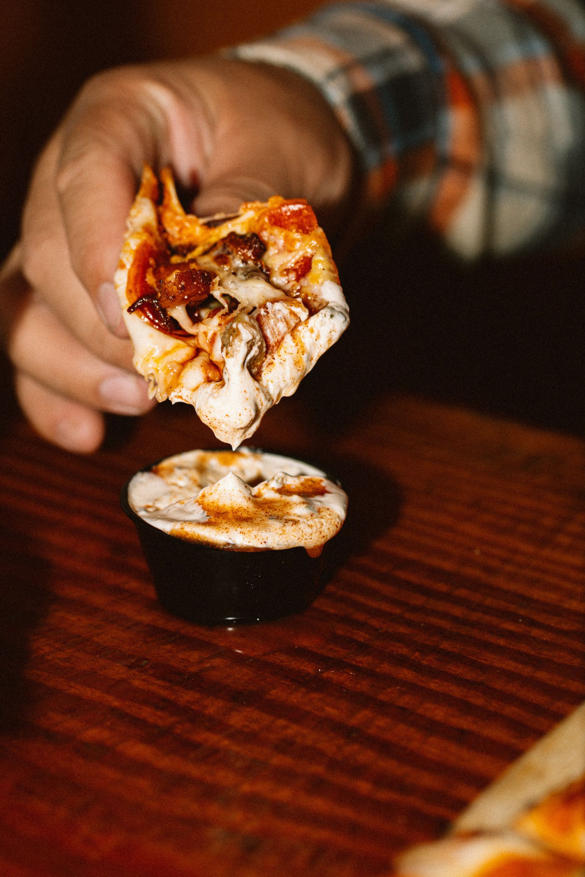 Hand holding a loaded mini pizza slice over a small pizza on a wooden table