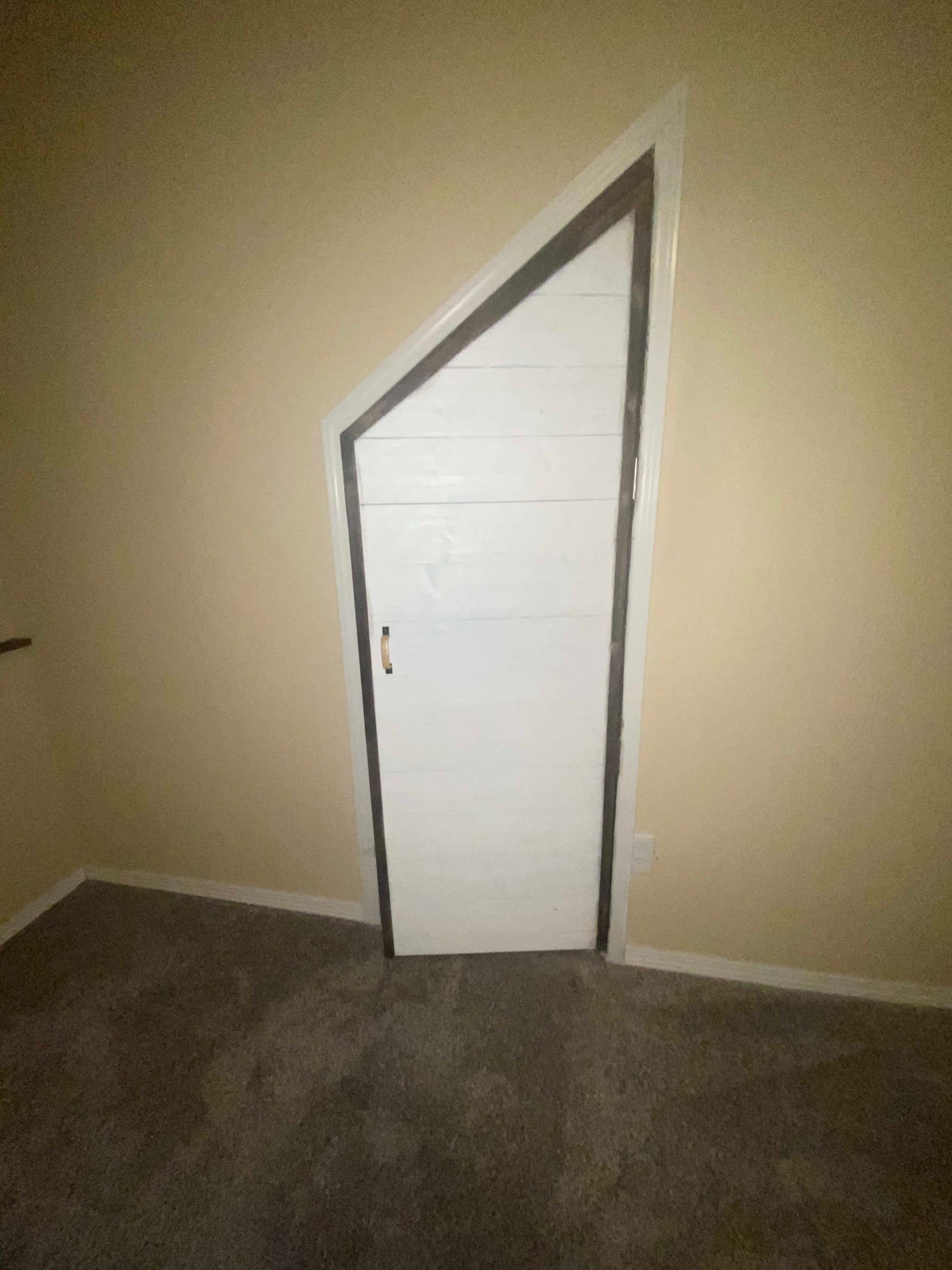 Small white slanted door in a beige room with dark carpeted floor