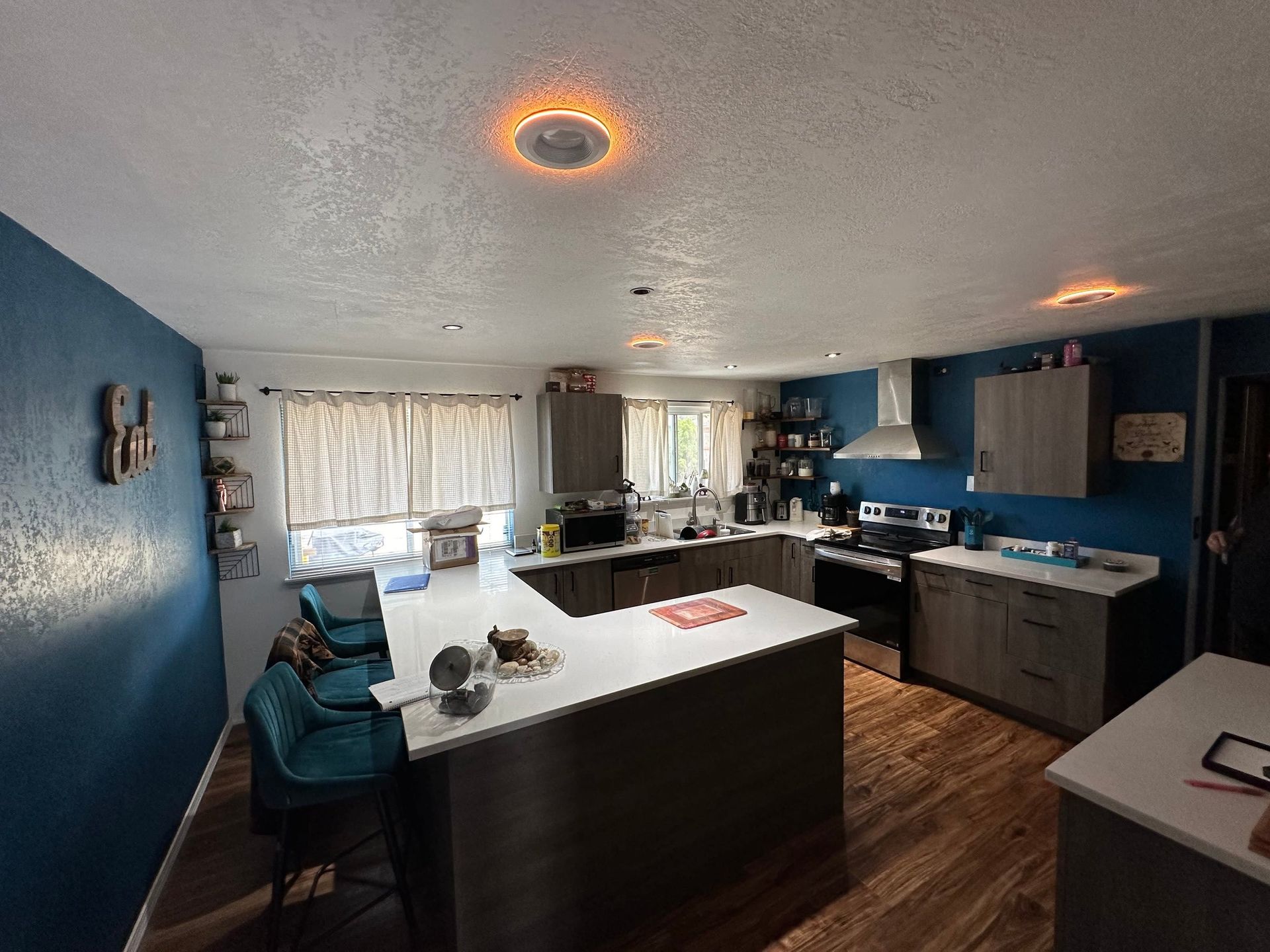 Modern blue-and-white kitchen with island, stainless appliances, wood floors, and warm ceiling lights