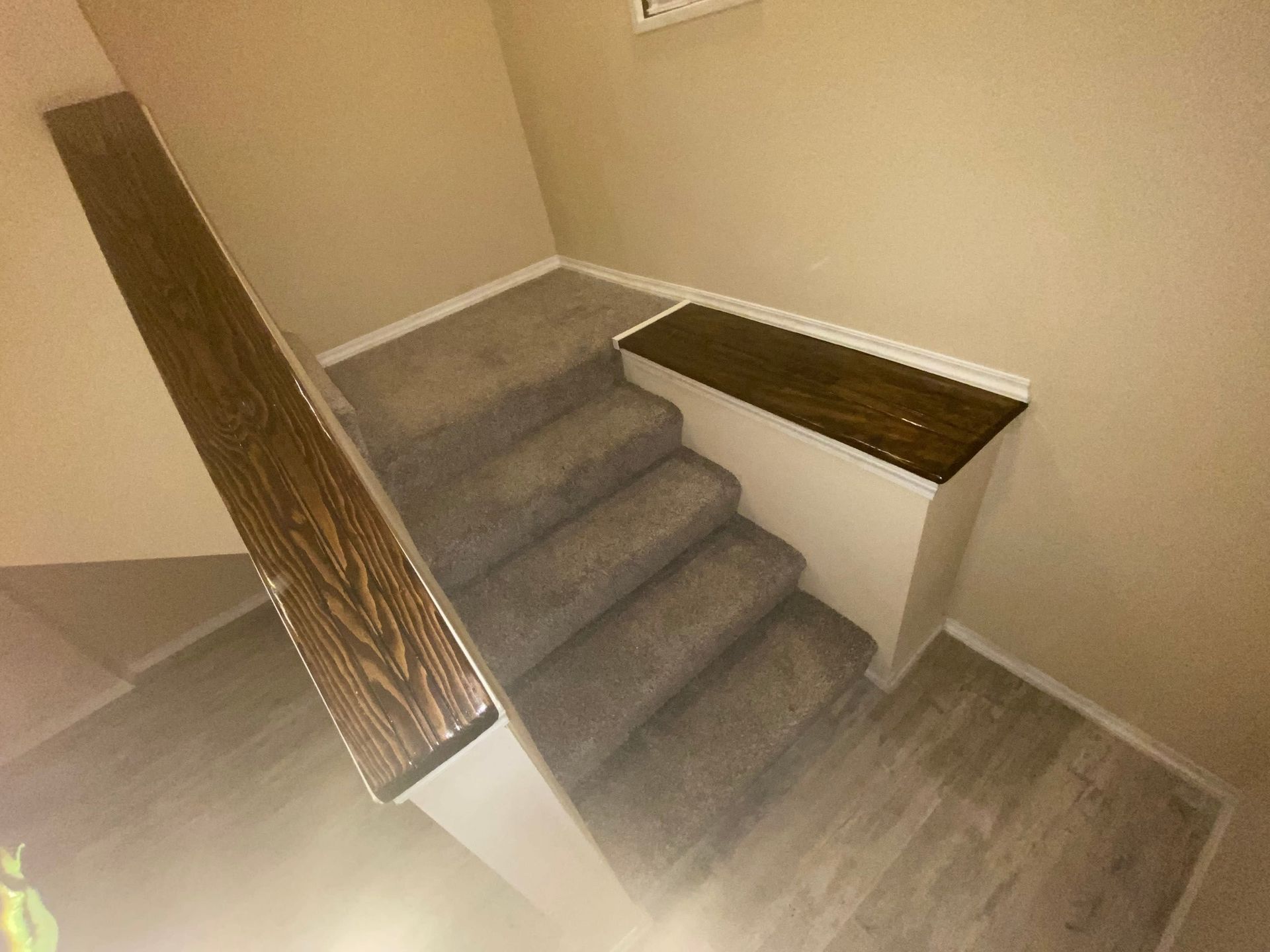 Staircase with gray carpet and wood handrails in a beige interior hallway