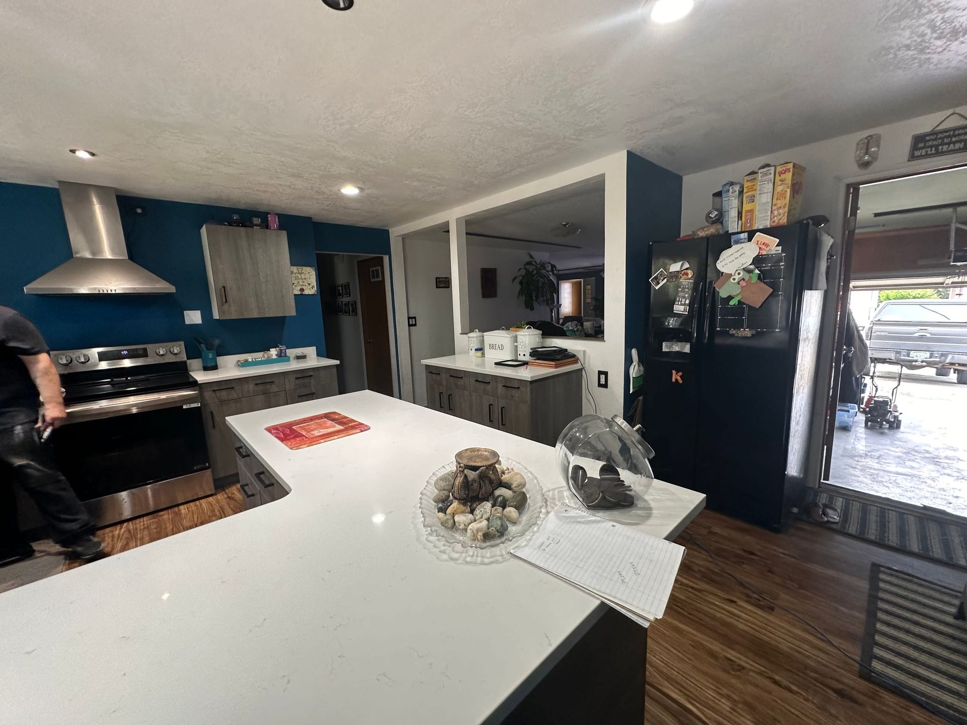 Modern kitchen with white island, black refrigerator, wood floors, and a person cooking by the stove
