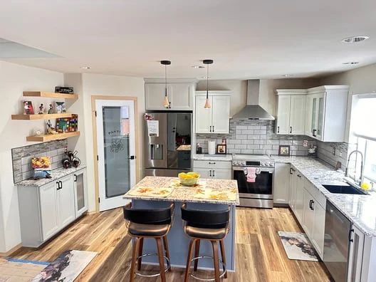 Modern kitchen with island, stools, stainless appliances, white cabinets, and wood floors