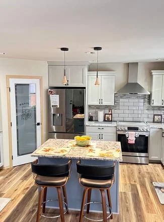 Modern kitchen with island, two black stools, white cabinets, stainless appliances, and subway tile backsplash