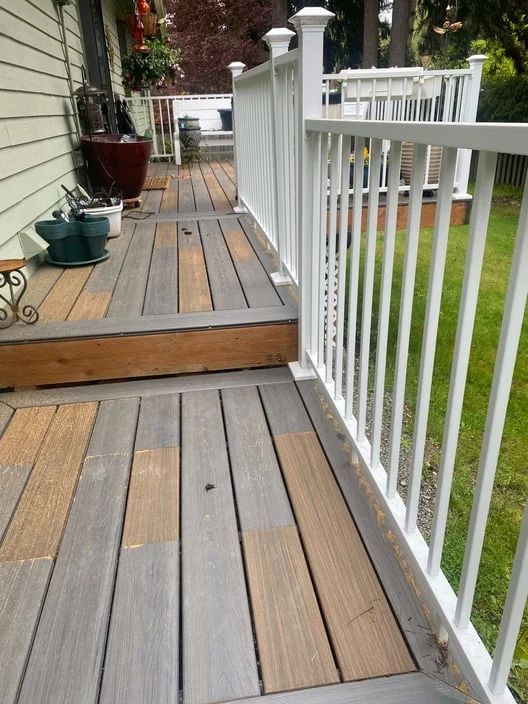 Wooden deck walkway with white railing and steps beside a house and lawn