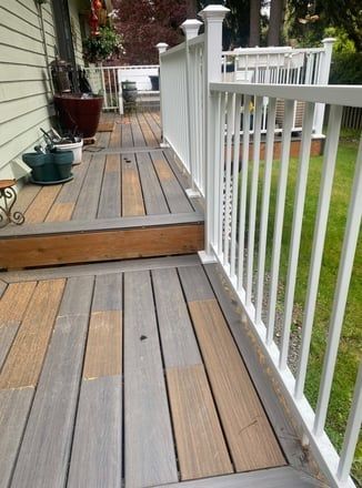 Wooden backyard deck with white railing, potted plants, and a short step up to a higher walkway