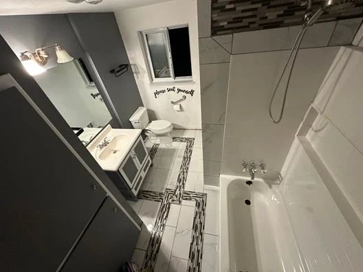 Modern bathroom with double vanity, large mirror, tiled floor, and white bathtub with shower curtain and wall tile accents