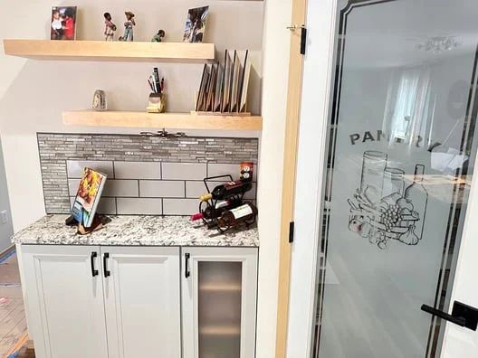 Small kitchen counter with shelves, white cabinets, granite top, and decorative items by a glass door