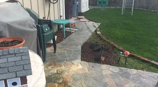 Patio beside a lawn with a broken stone edge and a small hole near the walkway