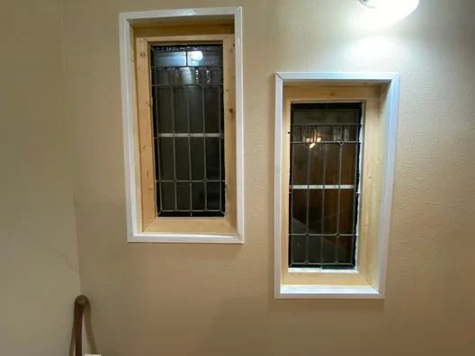 Two small rectangular windows with white trim on a beige wall, one above the other side by side.