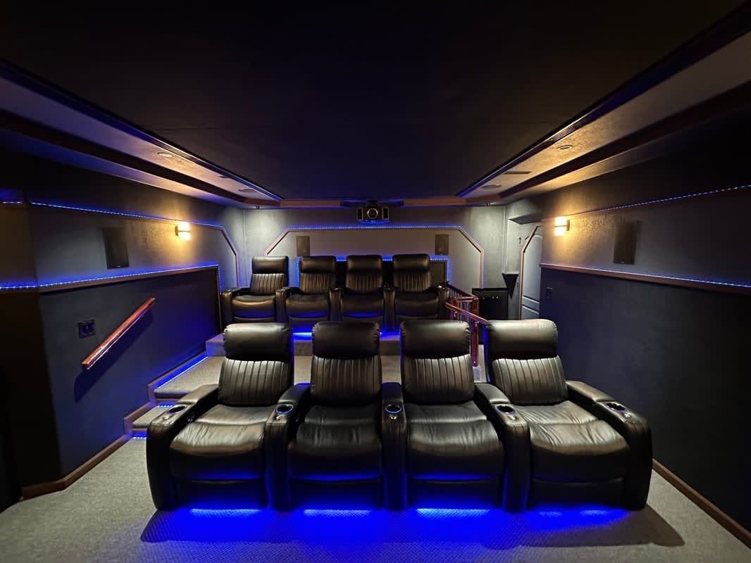 Luxury home theater with black leather recliners, blue accent lighting, and a large screen wall